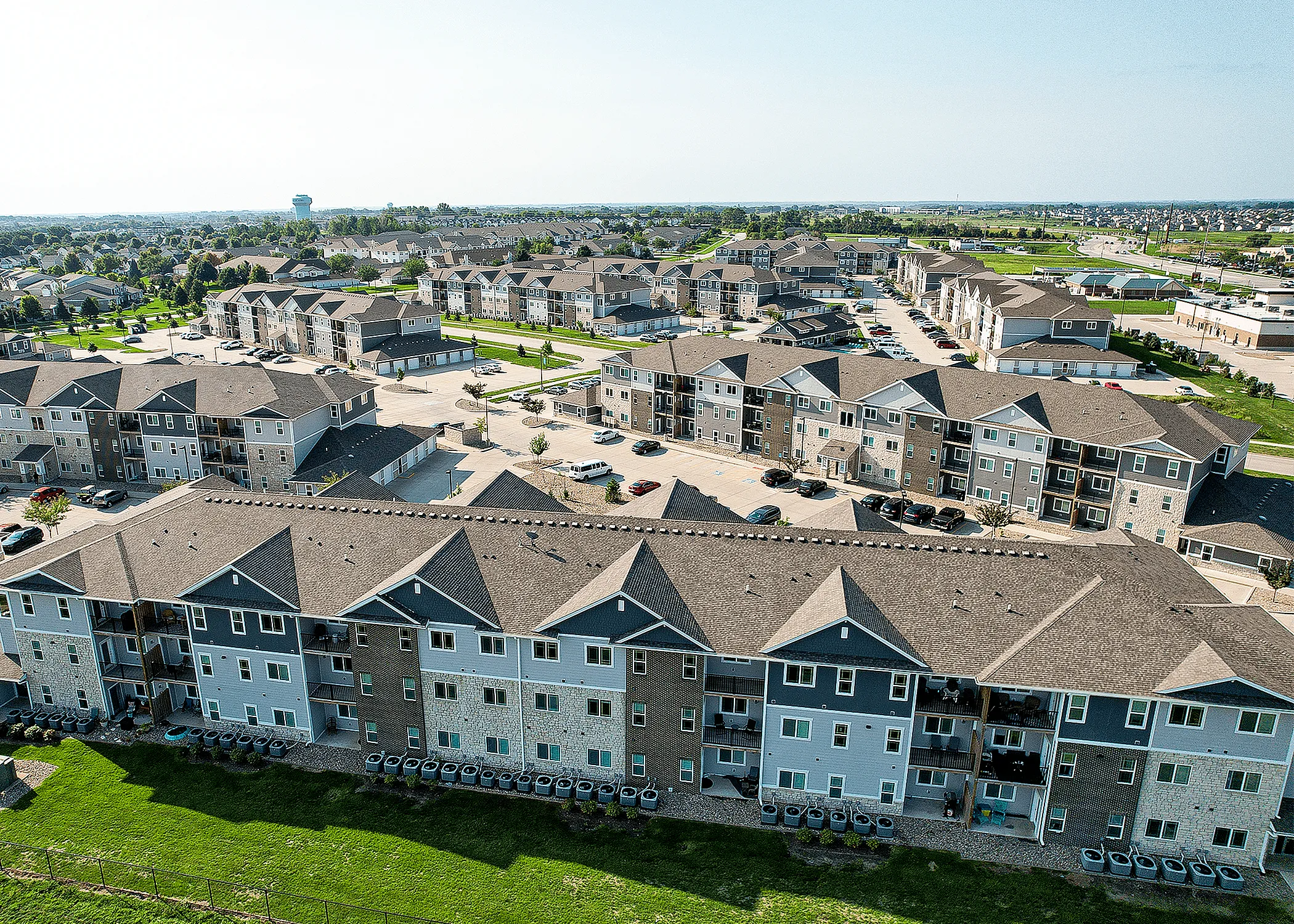 Expansive aerial view showcasing modern apartment complex with beautifully landscaped grounds and ample parking.