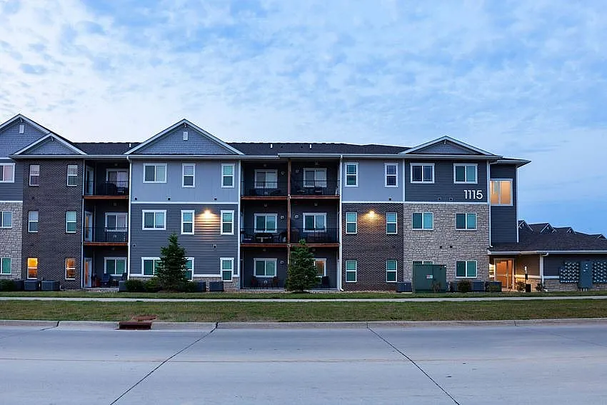 Modern three-story apartment building with stylish balconies and warm exterior lighting, set against a serene evening sky.