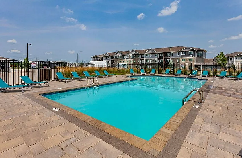 Inviting outdoor pool area with modern loungers, surrounded by charming apartment buildings under a clear blue sky.