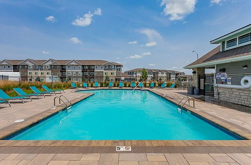 Inviting outdoor pool area with turquoise lounge chairs, perfect for summer relaxation, set against a backdrop of charming apartment buildings under a bright blue sky.
