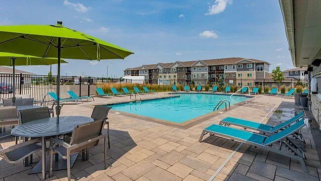 Luxurious apartment complex featuring a sparkling outdoor pool, modern lounge chairs, and vibrant green umbrellas, perfect for relaxation and social gatherings.