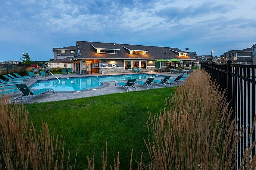 Elegant apartment complex with a beautifully lit pool area surrounded by stylish loungers and lush greenery, highlighting luxury living.