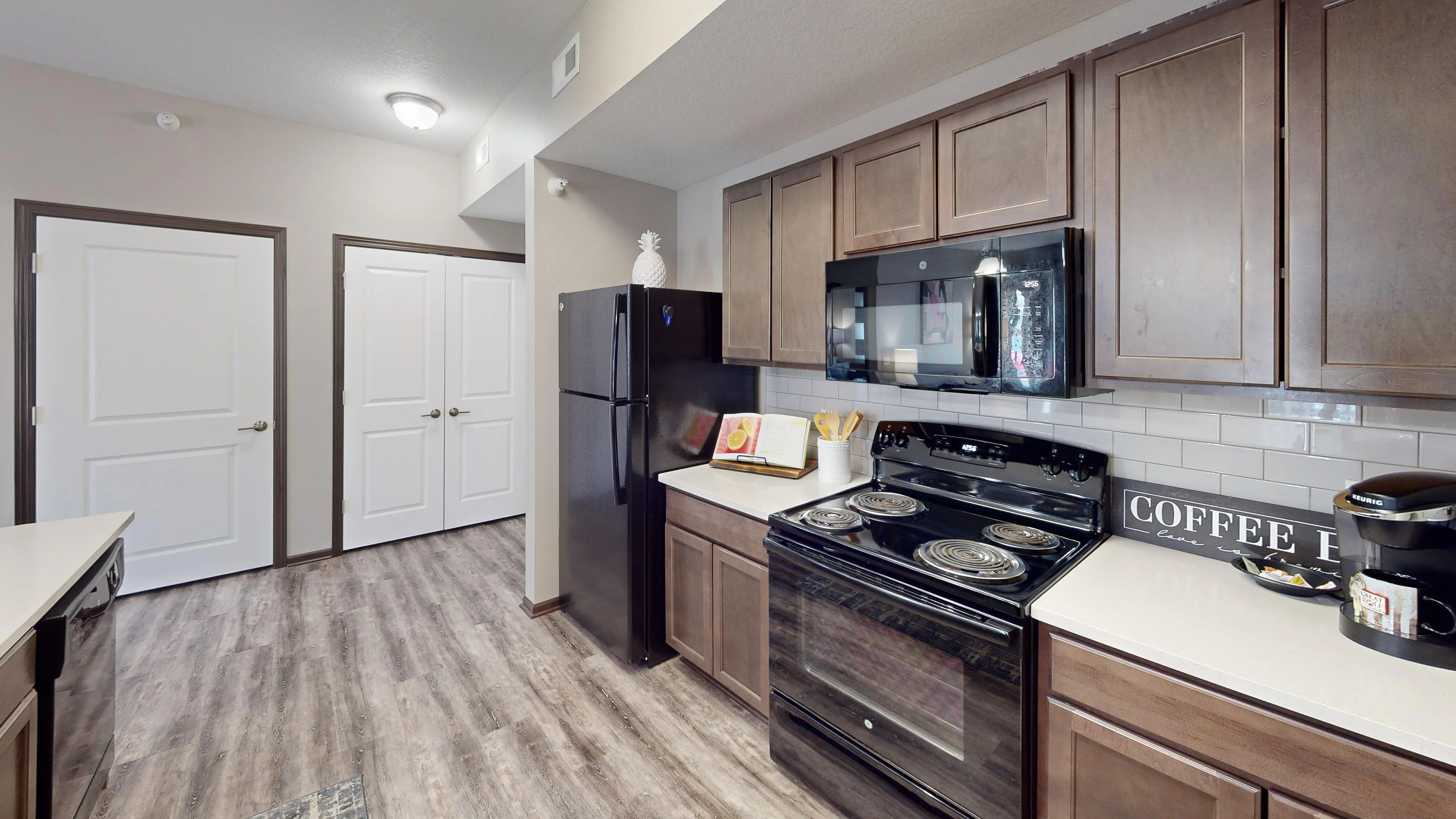 Modern kitchen featuring sleek black appliances, warm wooden cabinets, and elegant wood-style flooring.