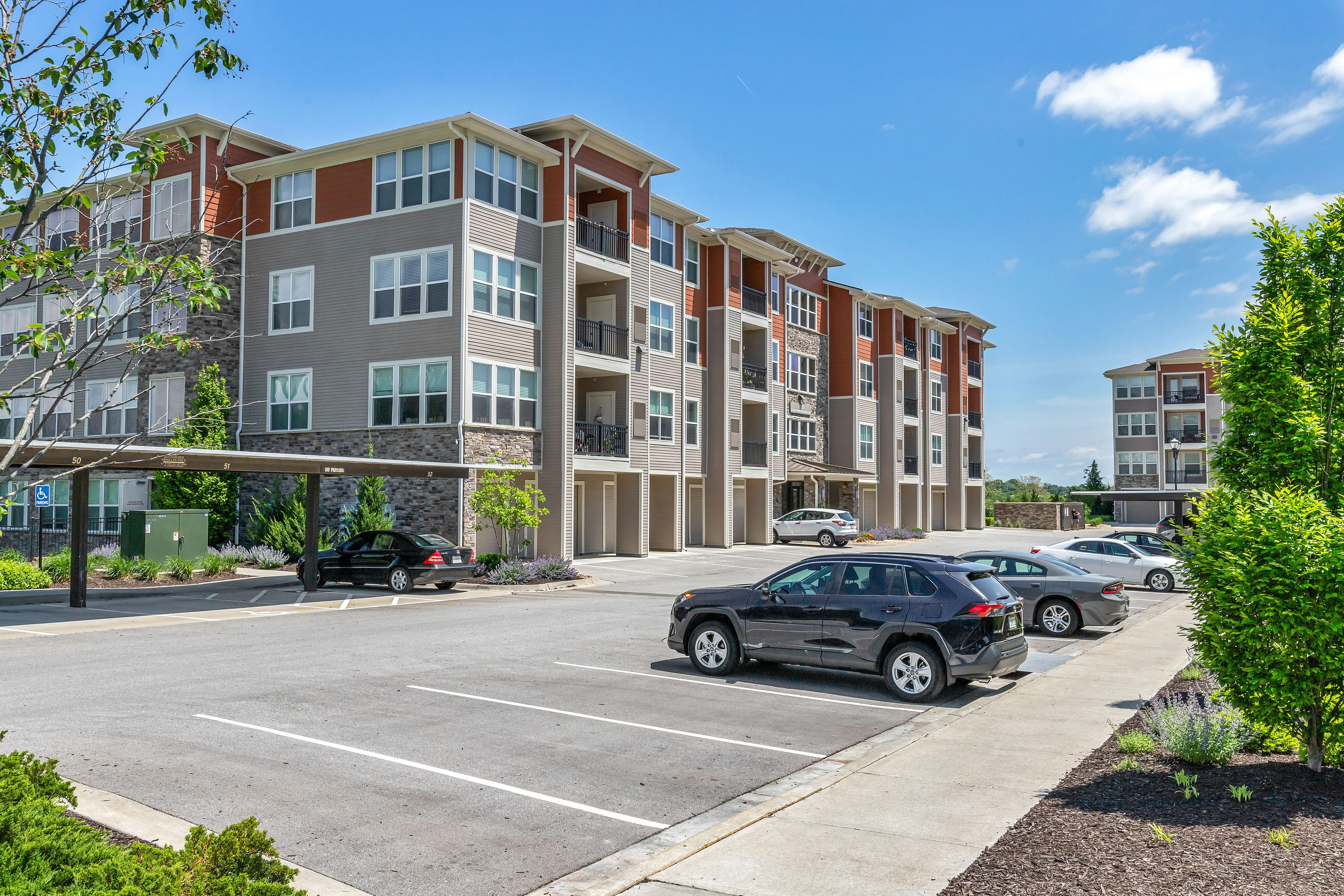 Modern apartment complex showcasing multi-story buildings with stylish facades and ample parking, set against a clear blue sky.