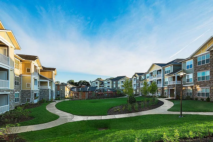 Elegant apartment complex with modern architecture surrounded by lush green lawns and scenic walkways under a bright blue sky.