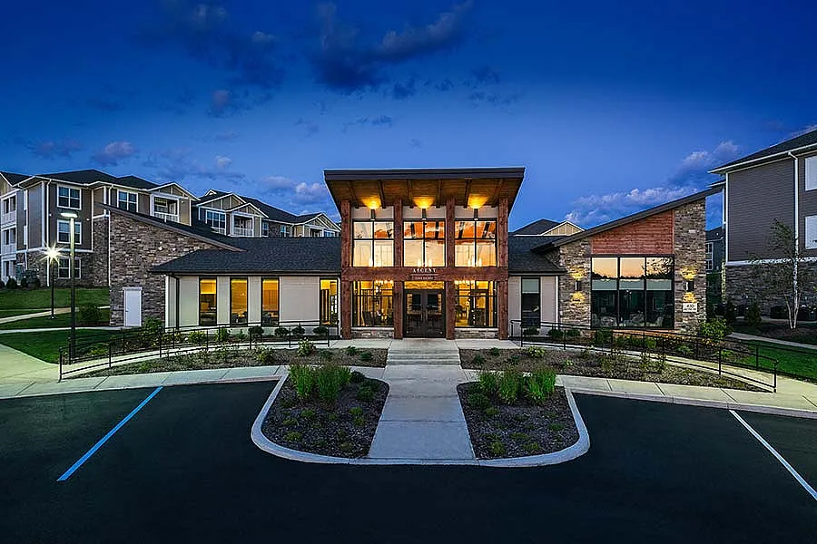 Elegant apartment complex illuminated at dusk, showcasing modern architecture with large windows and stone accents.