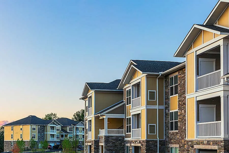 Modern apartment complex with elegant yellow and stone facade, featuring spacious balconies and scenic surroundings at sunset.