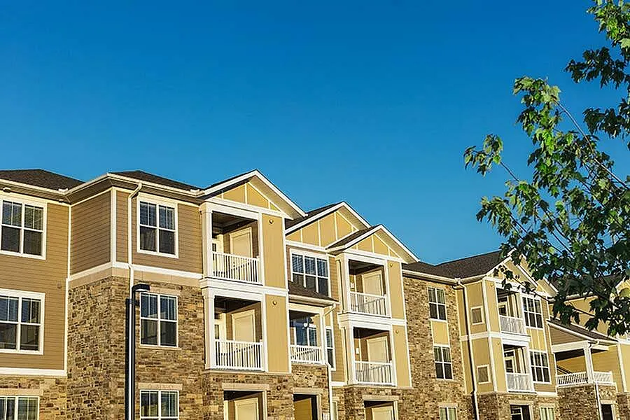 Charming apartment complex featuring modern architecture, spacious balconies, and surrounded by lush greenery under a clear blue sky.