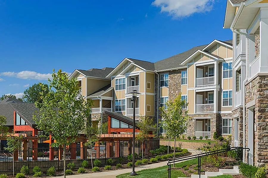 Charming multi-story residential buildings with modern architecture, surrounded by lush greenery and vibrant landscaping on a sunny day.