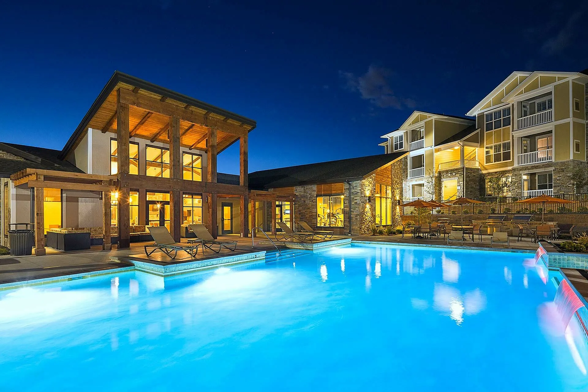 Luxurious poolside view at night with modern apartment complex featuring warm lighting and inviting lounge areas.