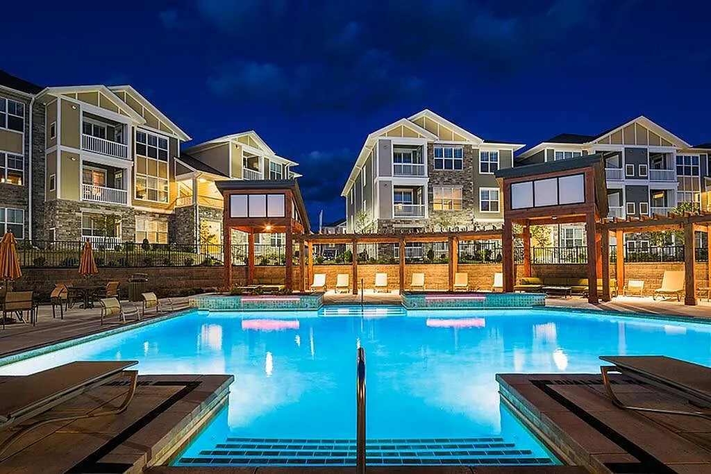 Luxurious apartment complex with a shimmering night-lit pool and elegant outdoor seating, showcasing modern architecture.