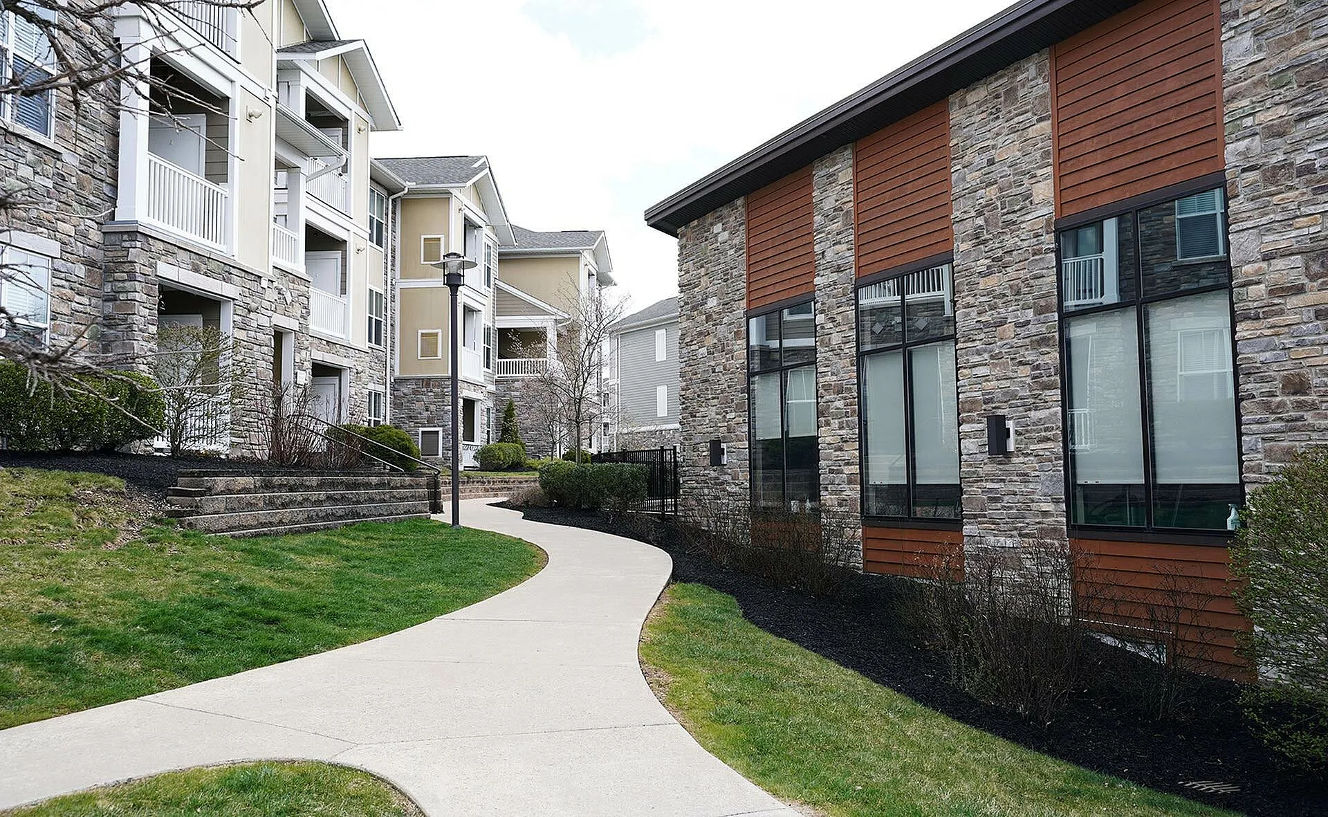 Modern apartment complex with elegant stone facades and lush green walkways, offering stylish and comfortable living spaces.