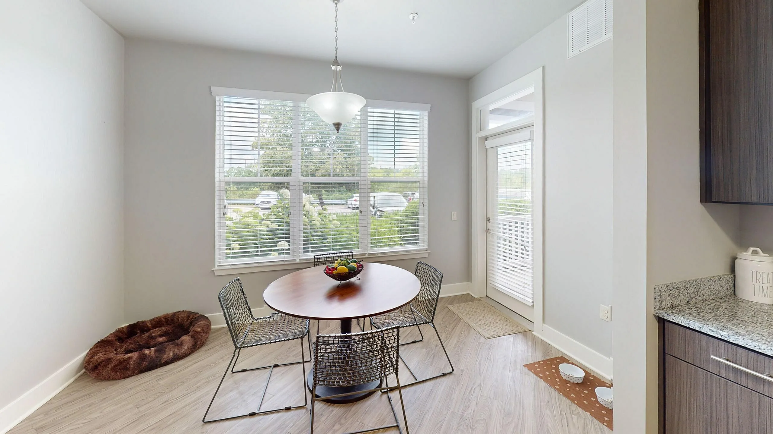 Bright dining area with a round wooden table, stylish chairs, large windows, and pet-friendly features.