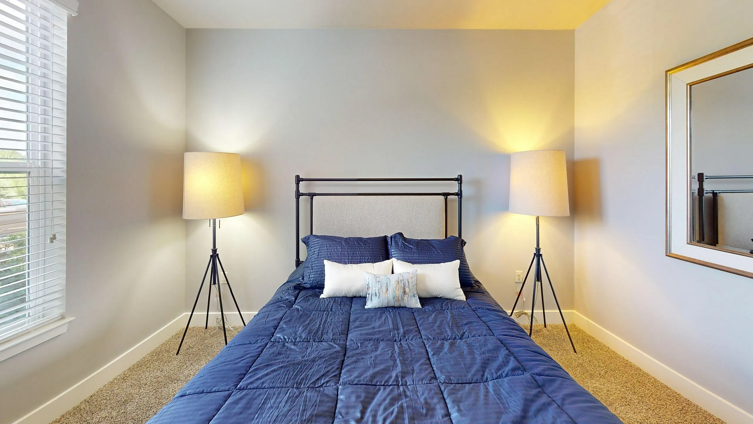 Inviting bedroom with stylish modern decor, featuring a cozy bed with blue bedding, elegant lamps, and a large window for natural light.