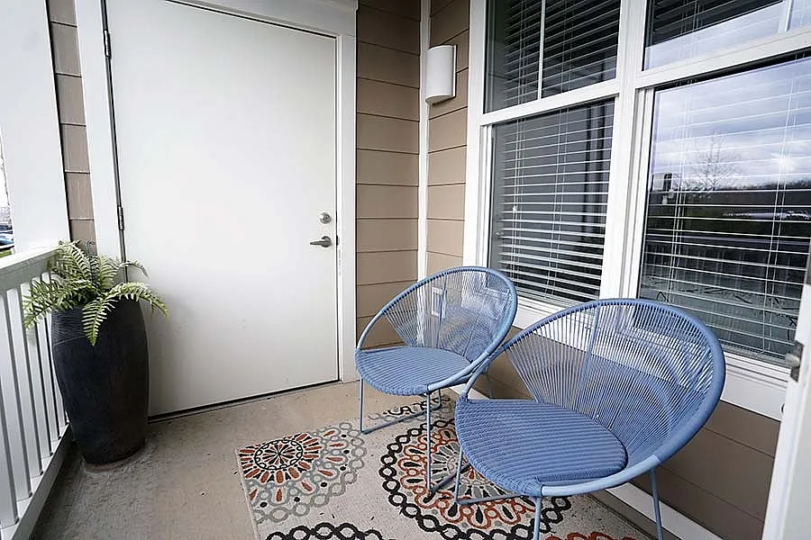 Charming balcony with modern blue chairs, vibrant patterned rug, and lush potted plant, perfect for relaxation.