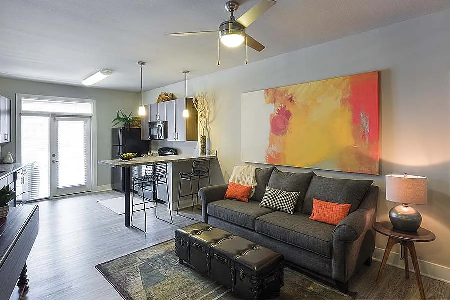 Modern open-concept living room with a stylish sofa, vibrant artwork, and cozy lighting leading into a chic kitchen with a breakfast bar.