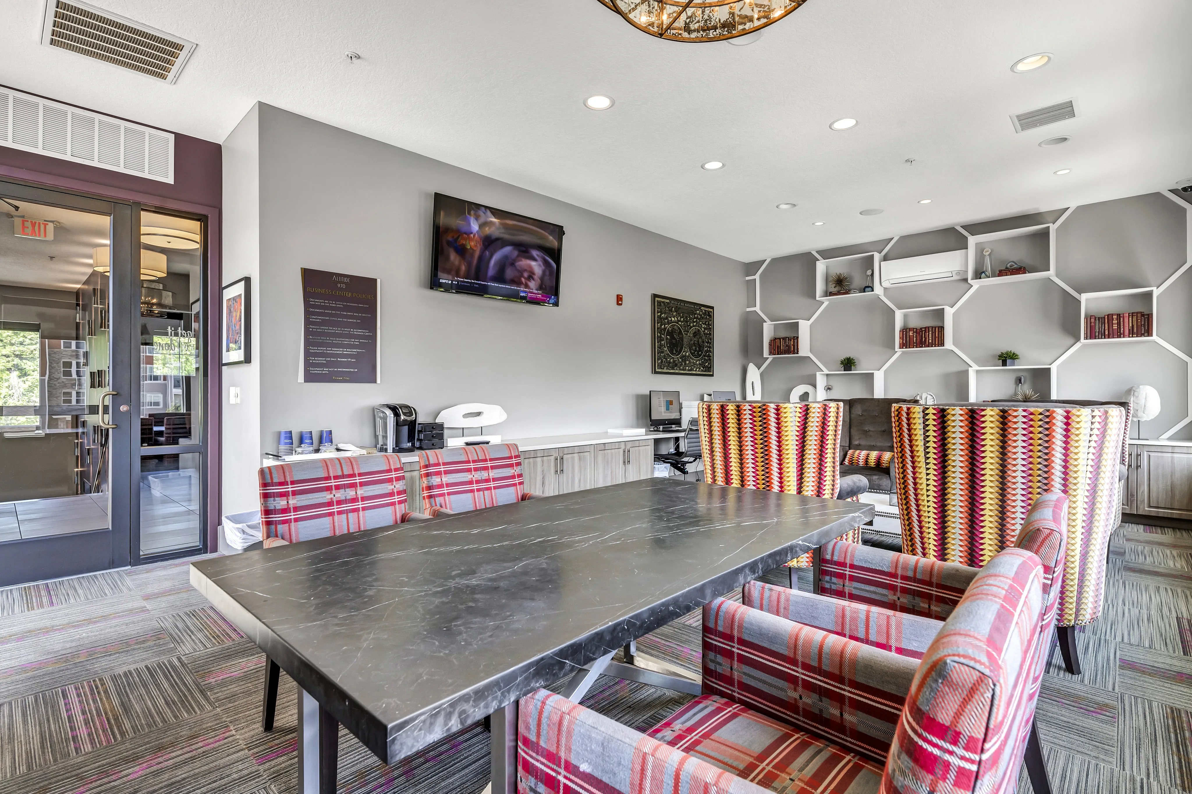 Modern communal space featuring a sleek marble table, vibrant plaid and patterned chairs, and honeycomb shelving with artistic decor.