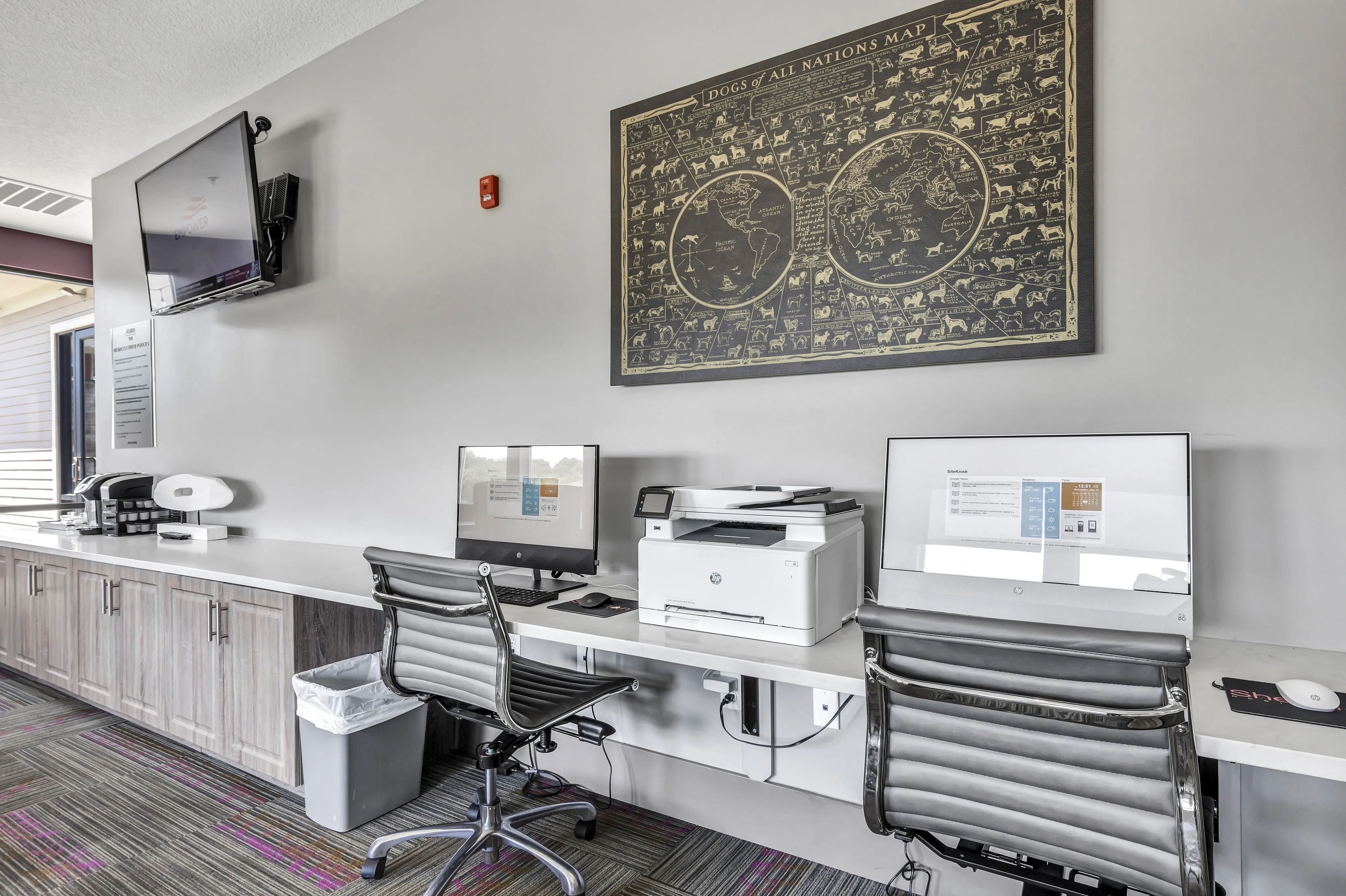 Modern office space with chic workstations, featuring sleek computers and a multifunction printer, complemented by a stylish wall map and vibrant carpet.