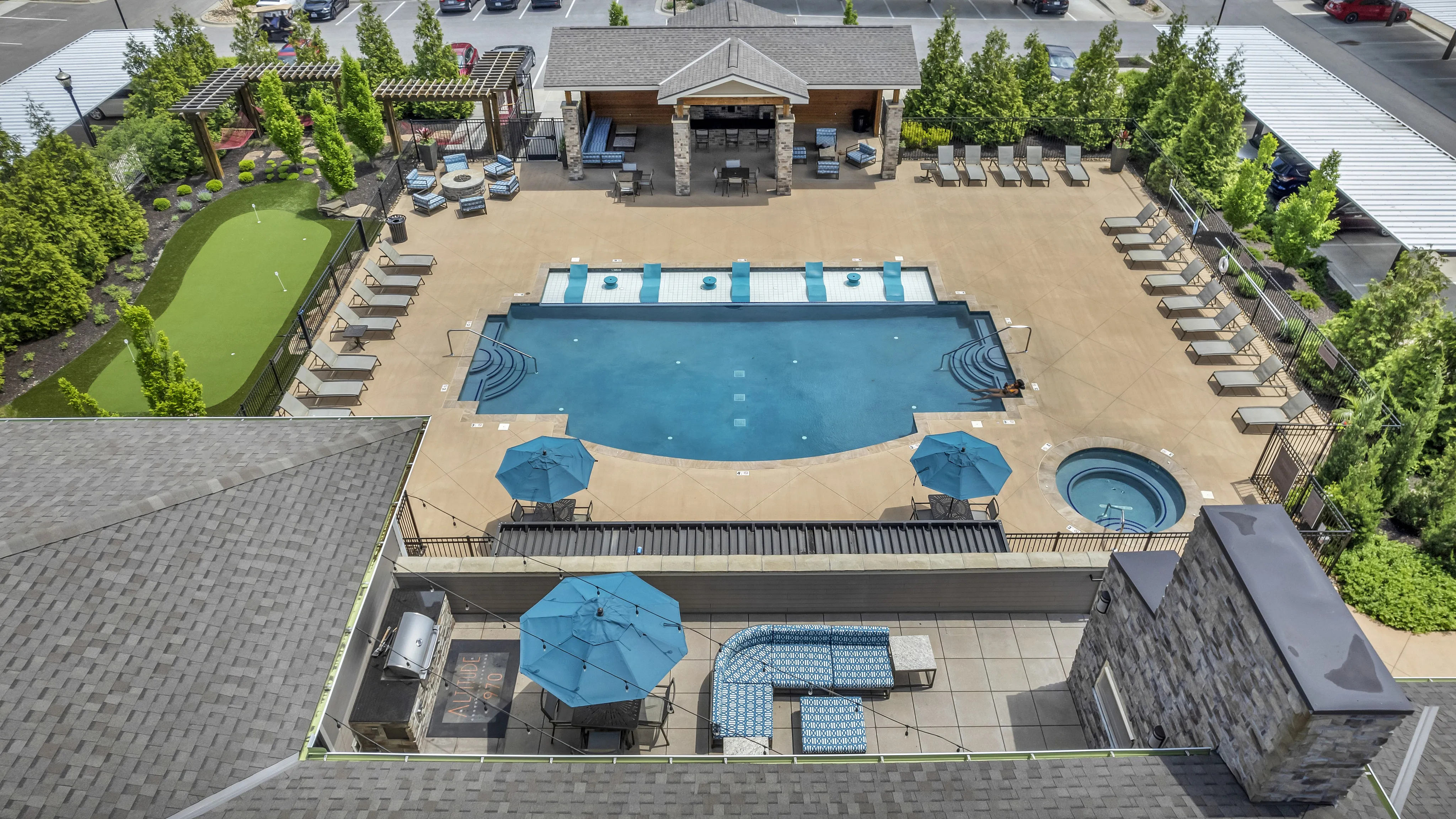 Luxurious apartment complex aerial view showcasing a shimmering pool, inviting lounge chairs, modern outdoor seating with blue umbrellas, and manicured greenery for a perfect oasis.