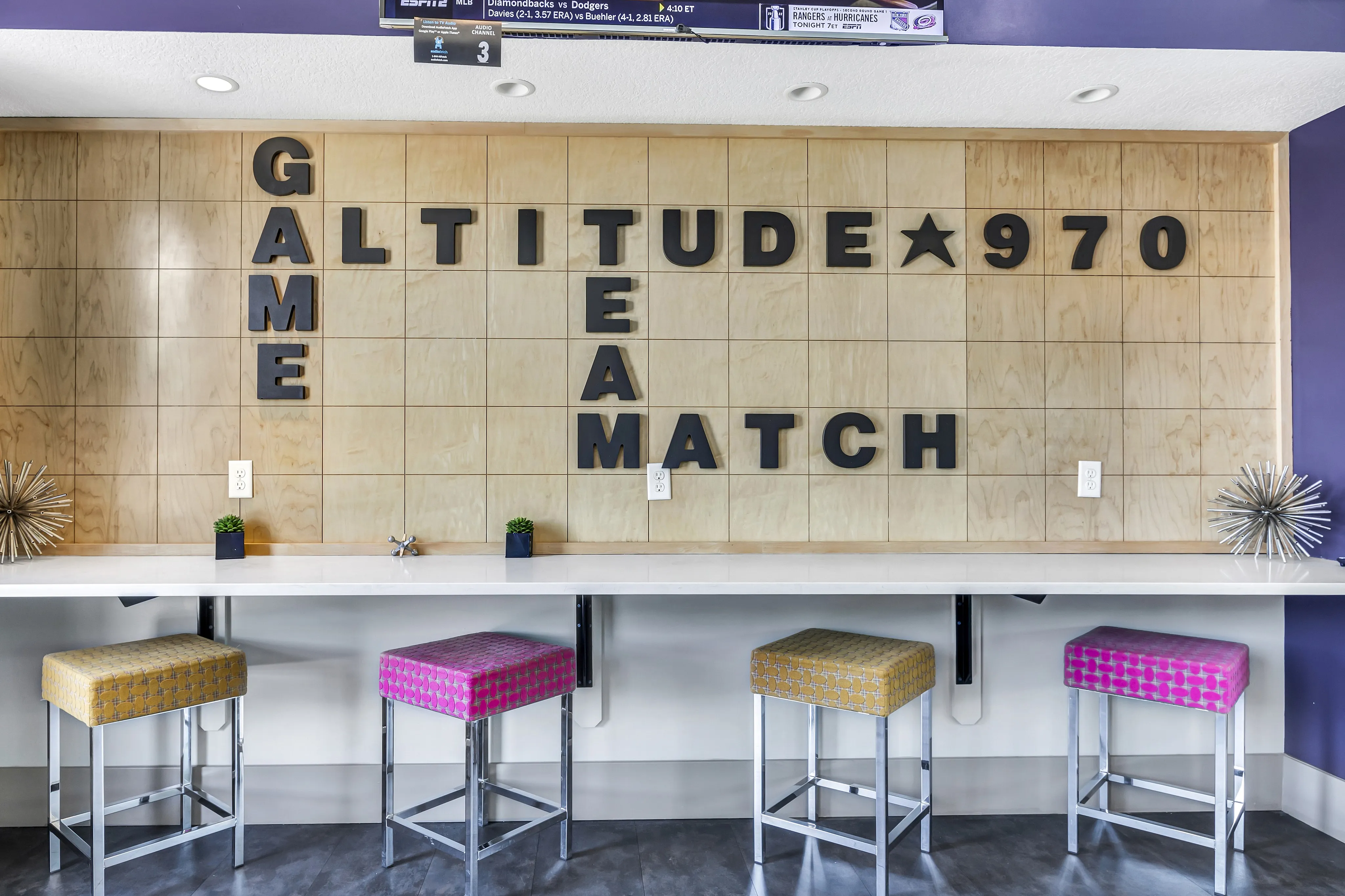 Chic community lounge with modern bar seating, playful wall decor spelling 'GAME,' and vibrant patterned stools for a fun and welcoming atmosphere.