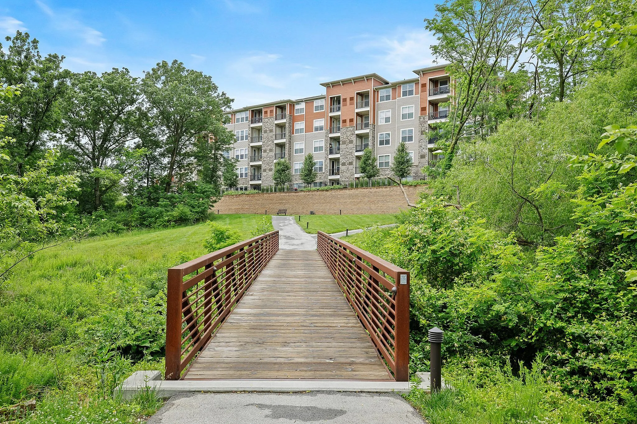 Charming apartment complex surrounded by lush greenery, featuring a scenic wooden bridge leading to a modern building.