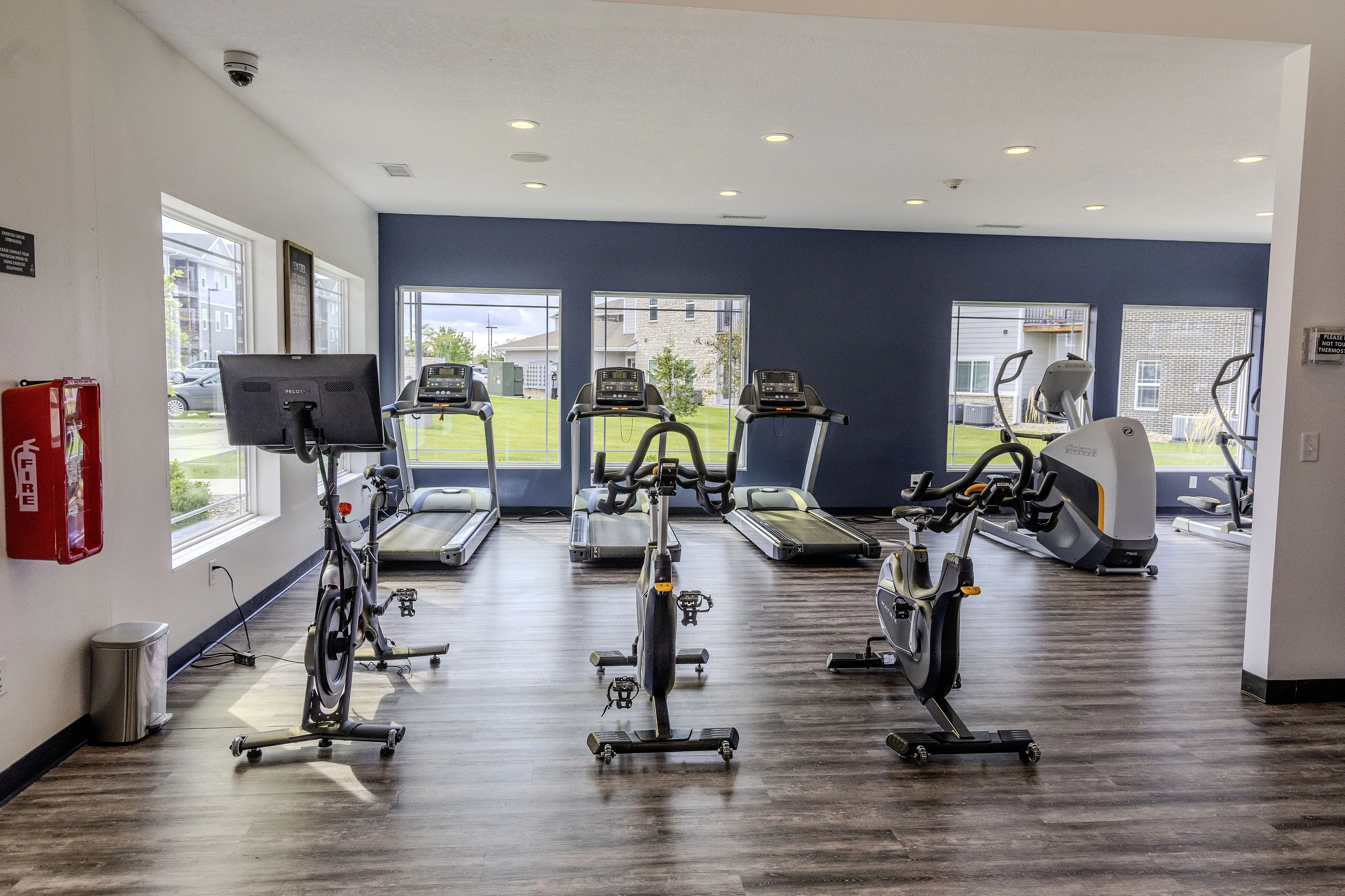 Bright modern gym with state-of-the-art exercise equipment, featuring treadmills and stationary bikes against a backdrop of large windows showcasing a lush outdoor view.