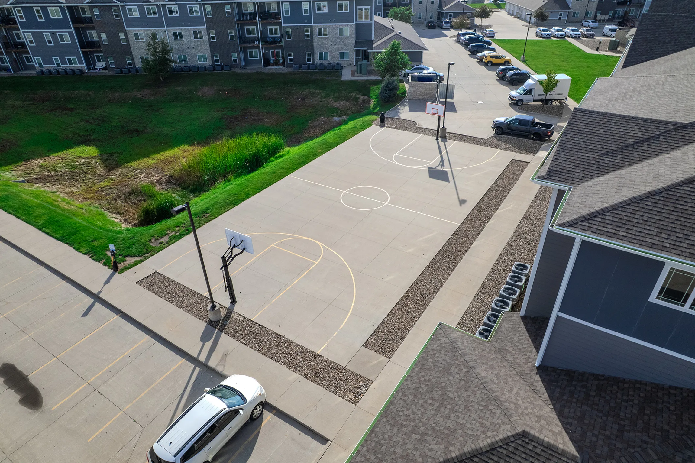 Aerial view of a well-maintained apartment complex featuring a spacious basketball court and ample parking, set against a backdrop of lush greenery.