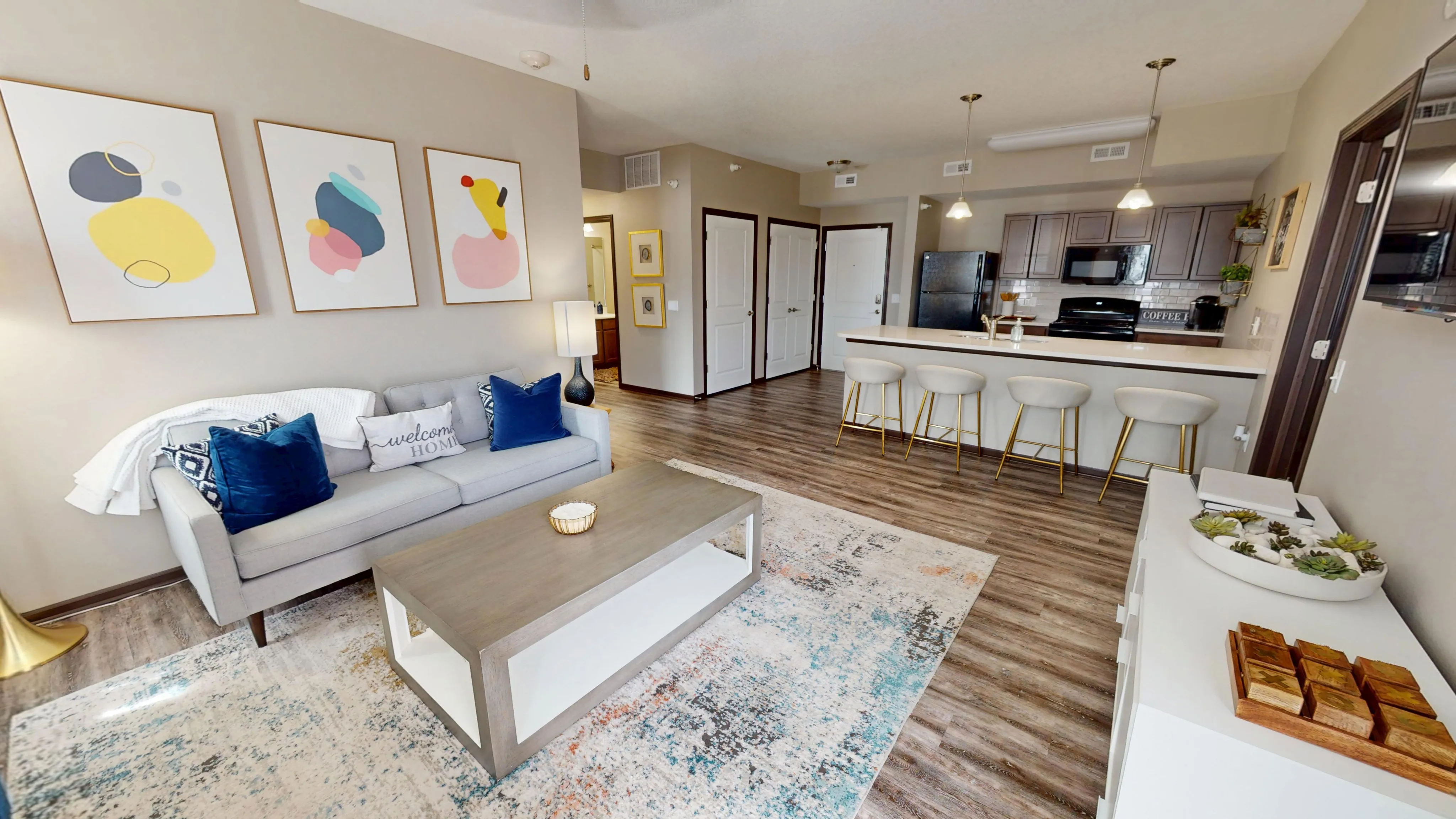 Modern open-plan living room and kitchen with stylish decor, featuring cozy seating, vibrant abstract art, and a sleek breakfast bar.