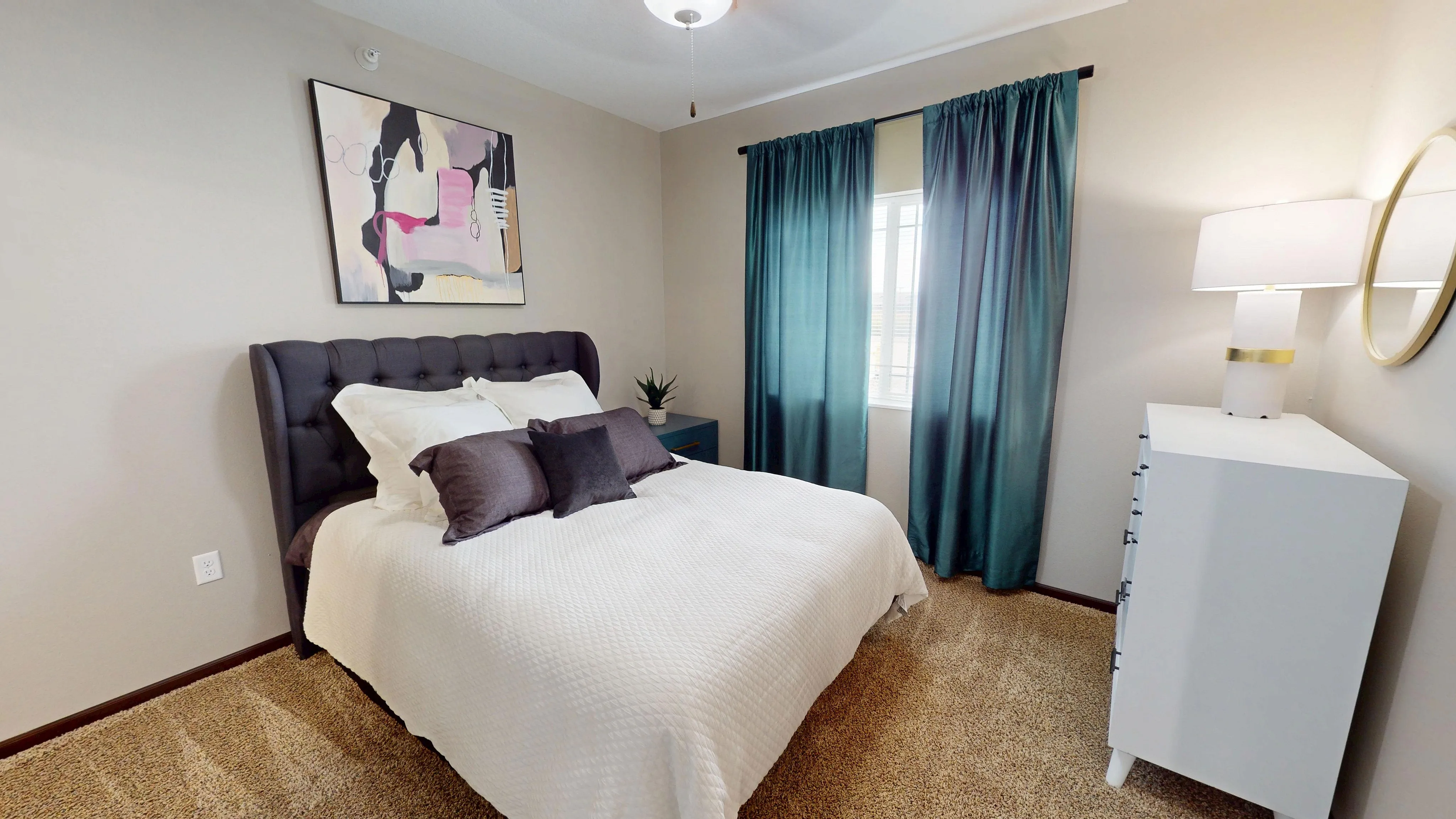 Inviting bedroom featuring a plush bed with a tufted headboard, contemporary artwork, and elegant teal curtains.