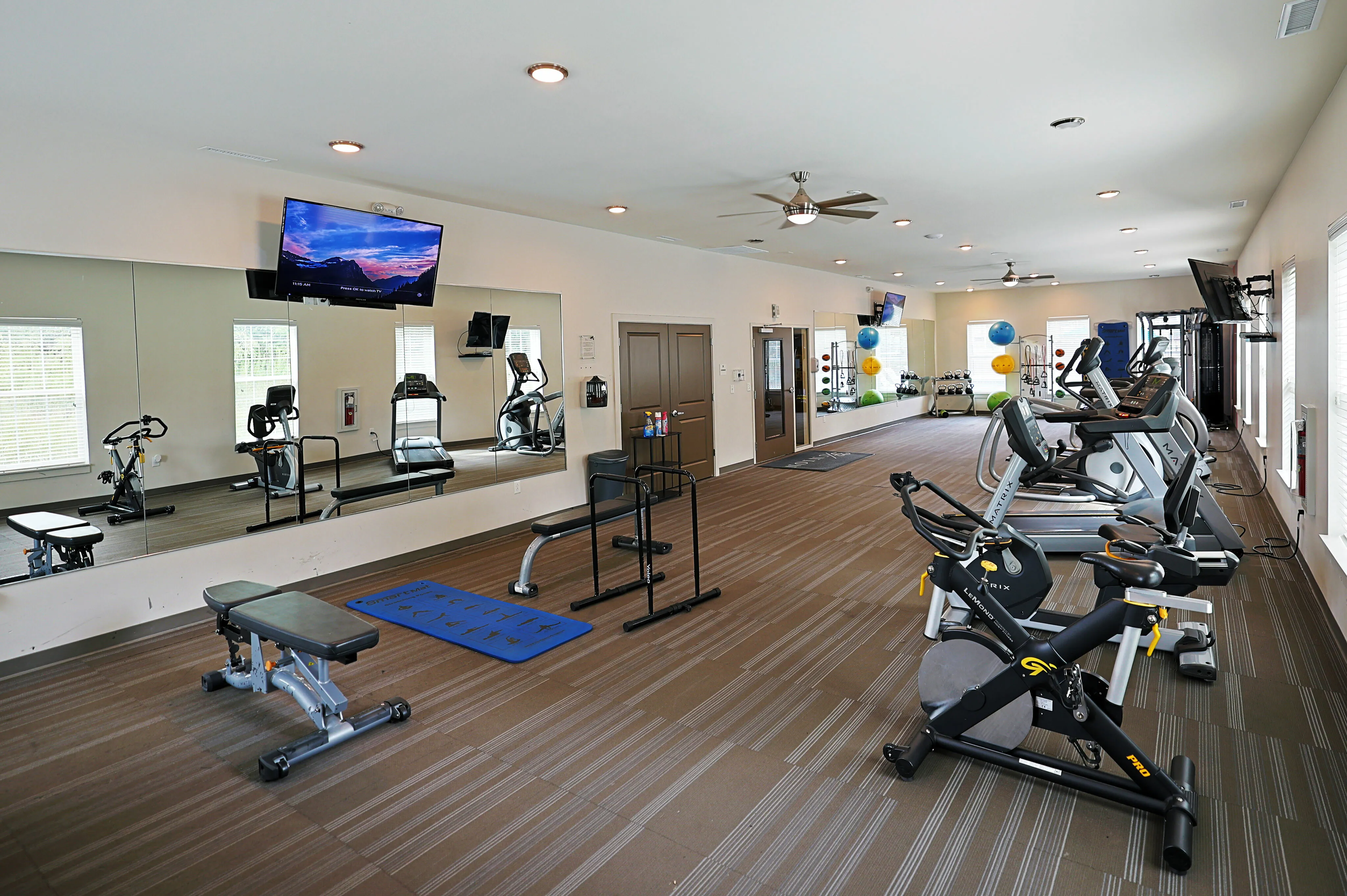 Spacious and bright fitness center with modern exercise equipment, large mirrors, and elegant lighting.
