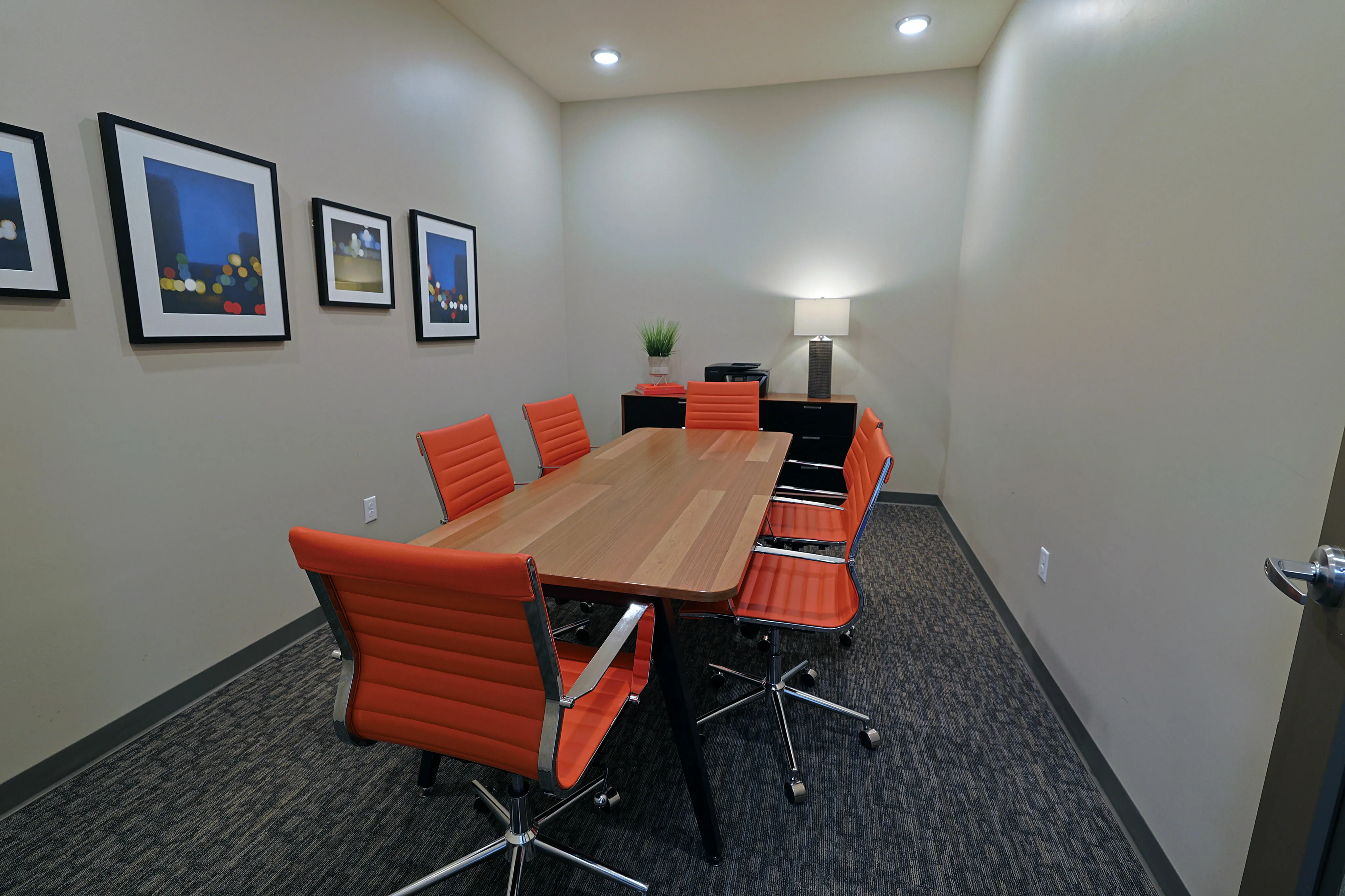 Modern conference room with vibrant orange chairs, sleek wooden table, and stylish artwork on the walls.