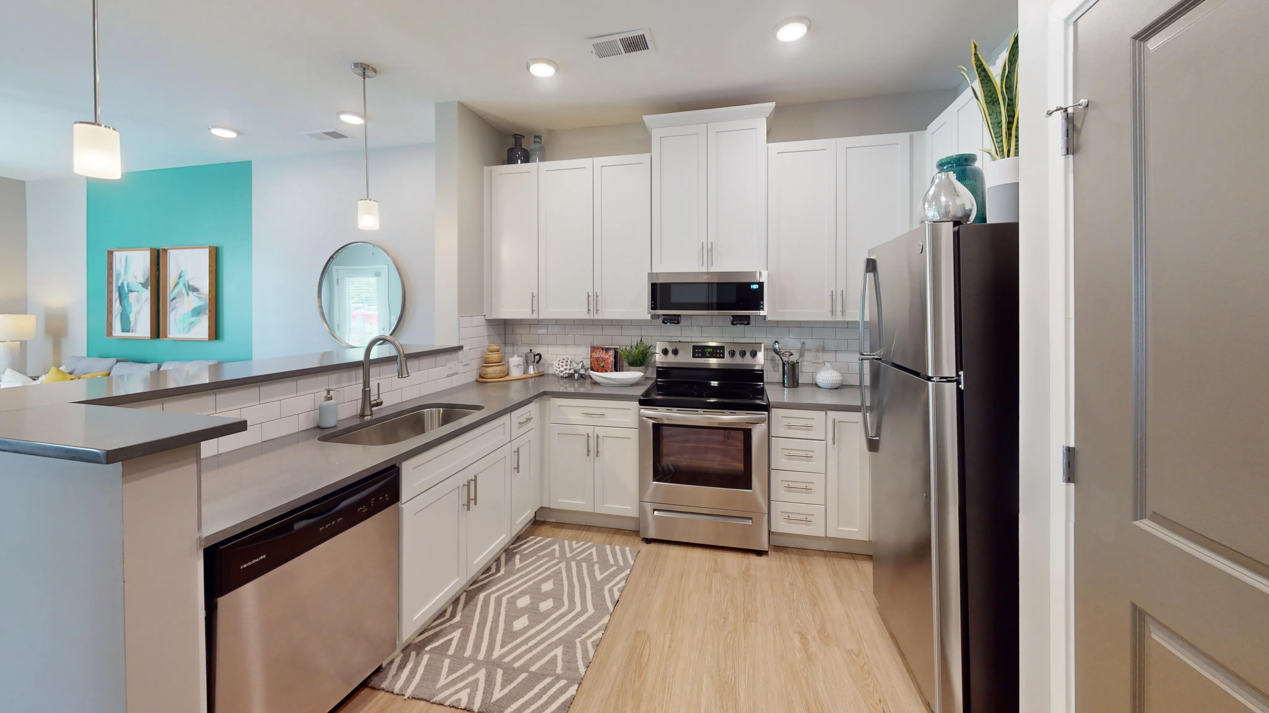Modern kitchen with sleek white cabinets, stainless steel appliances, and elegant pendant lighting, adjacent to a vibrant living area with stylish decor.