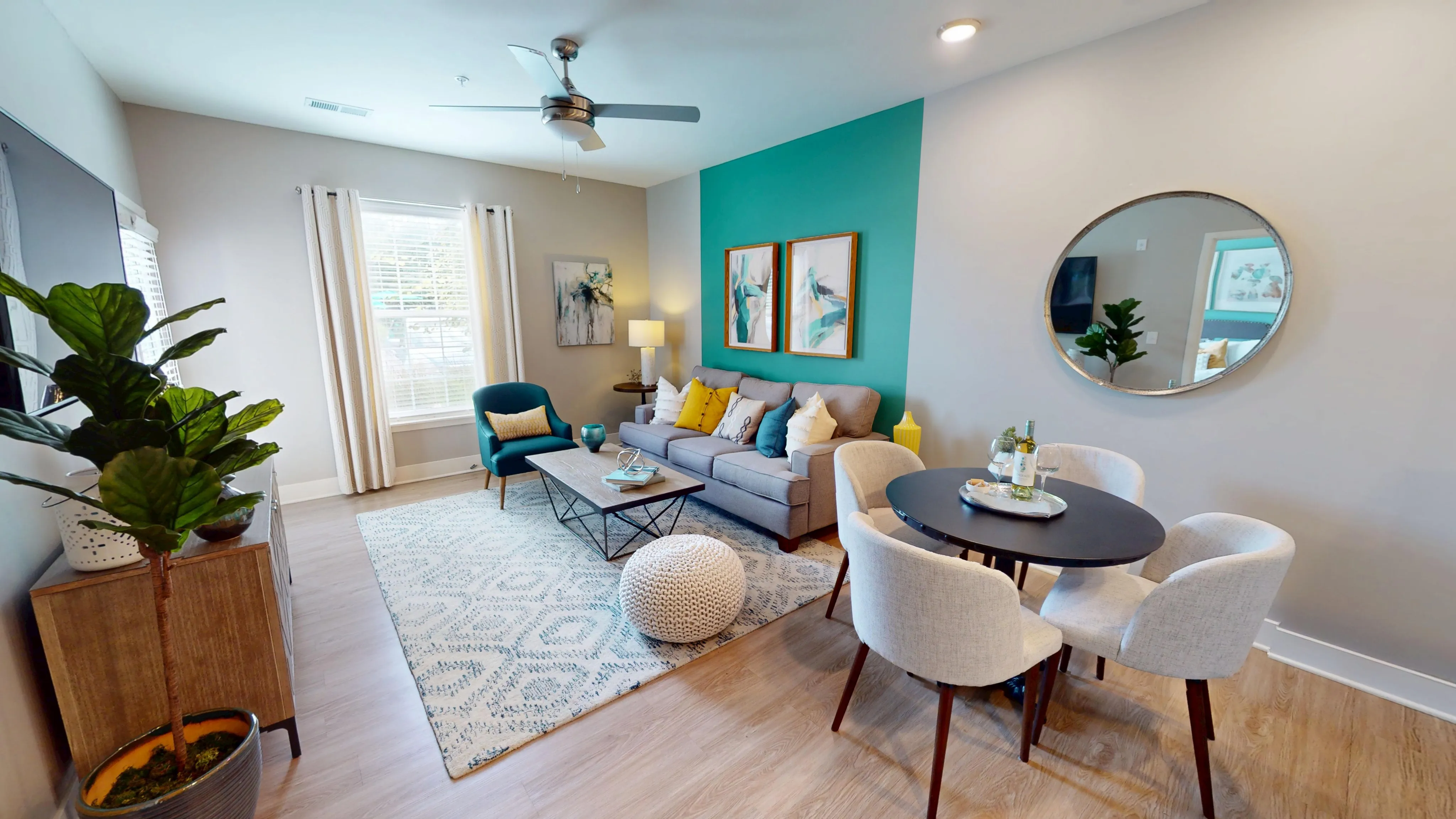 Inviting living space with modern decor, a cozy gray sofa, vibrant teal accent wall, and a stylish dining area.