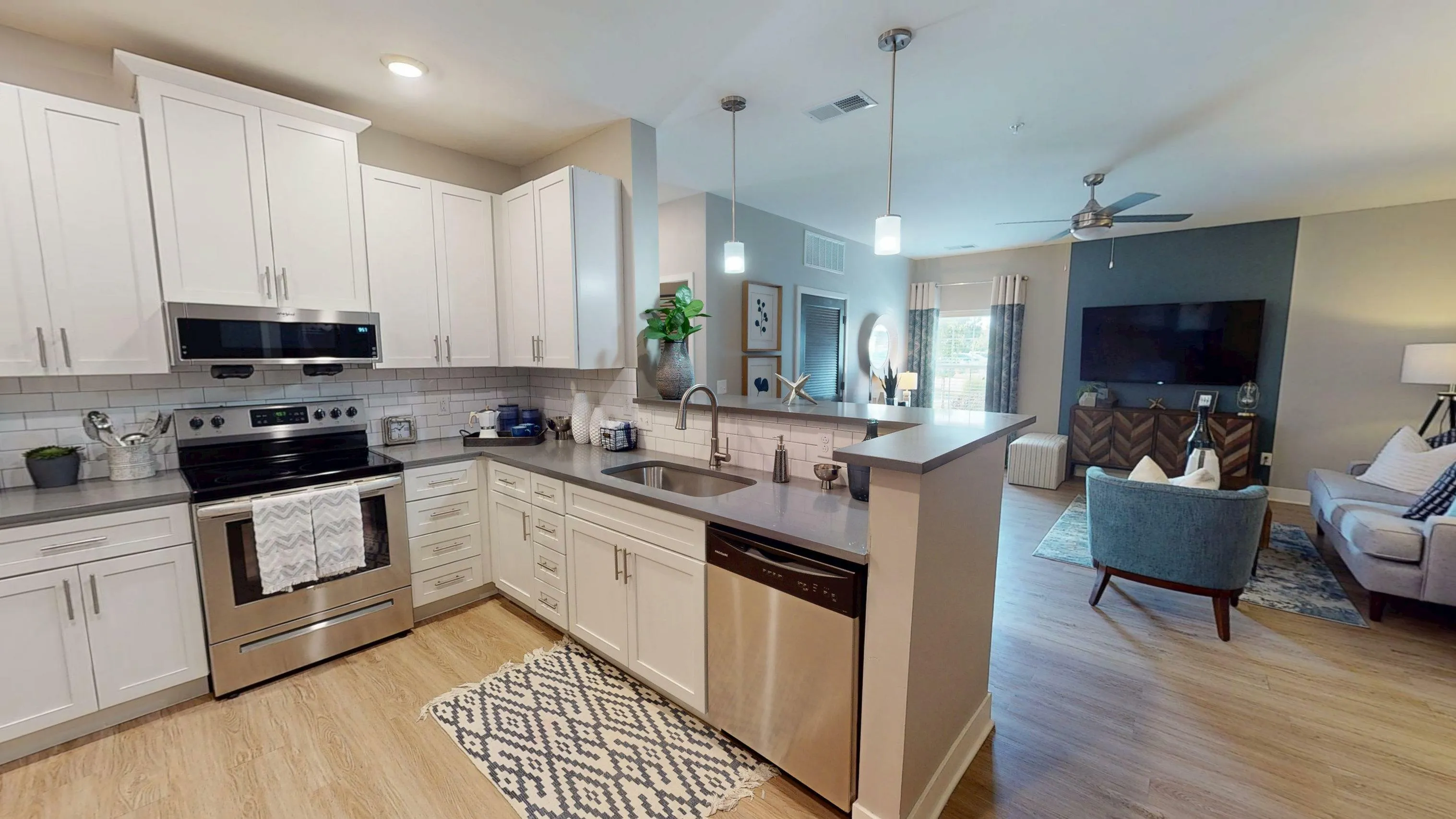 Modern open-plan kitchen and living room with sleek white cabinets, stainless steel appliances, and cozy seating area perfect for entertaining.