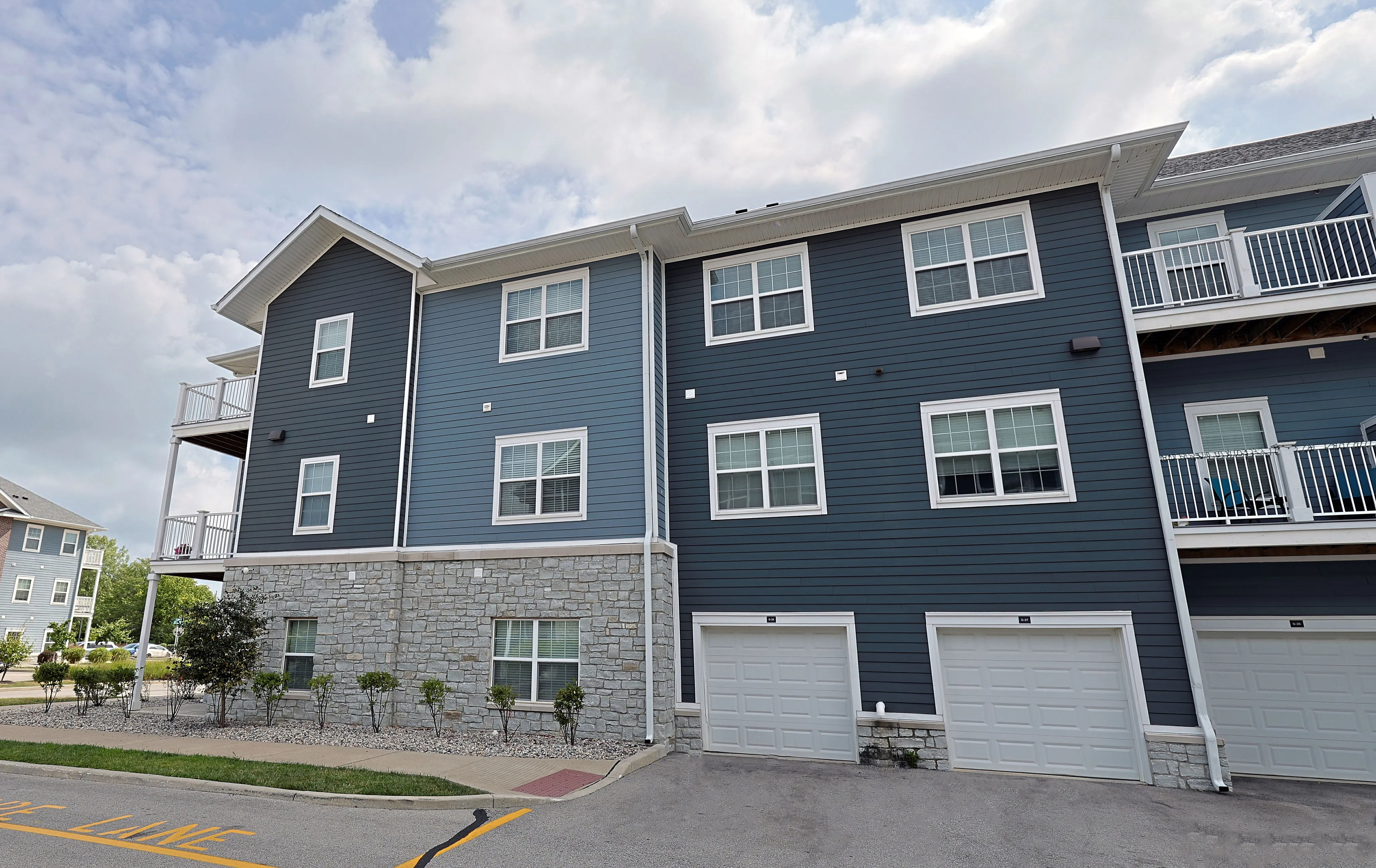 Modern apartment exterior with stylish blue siding, stone accents, and private balconies, offering a welcoming and upscale living environment.