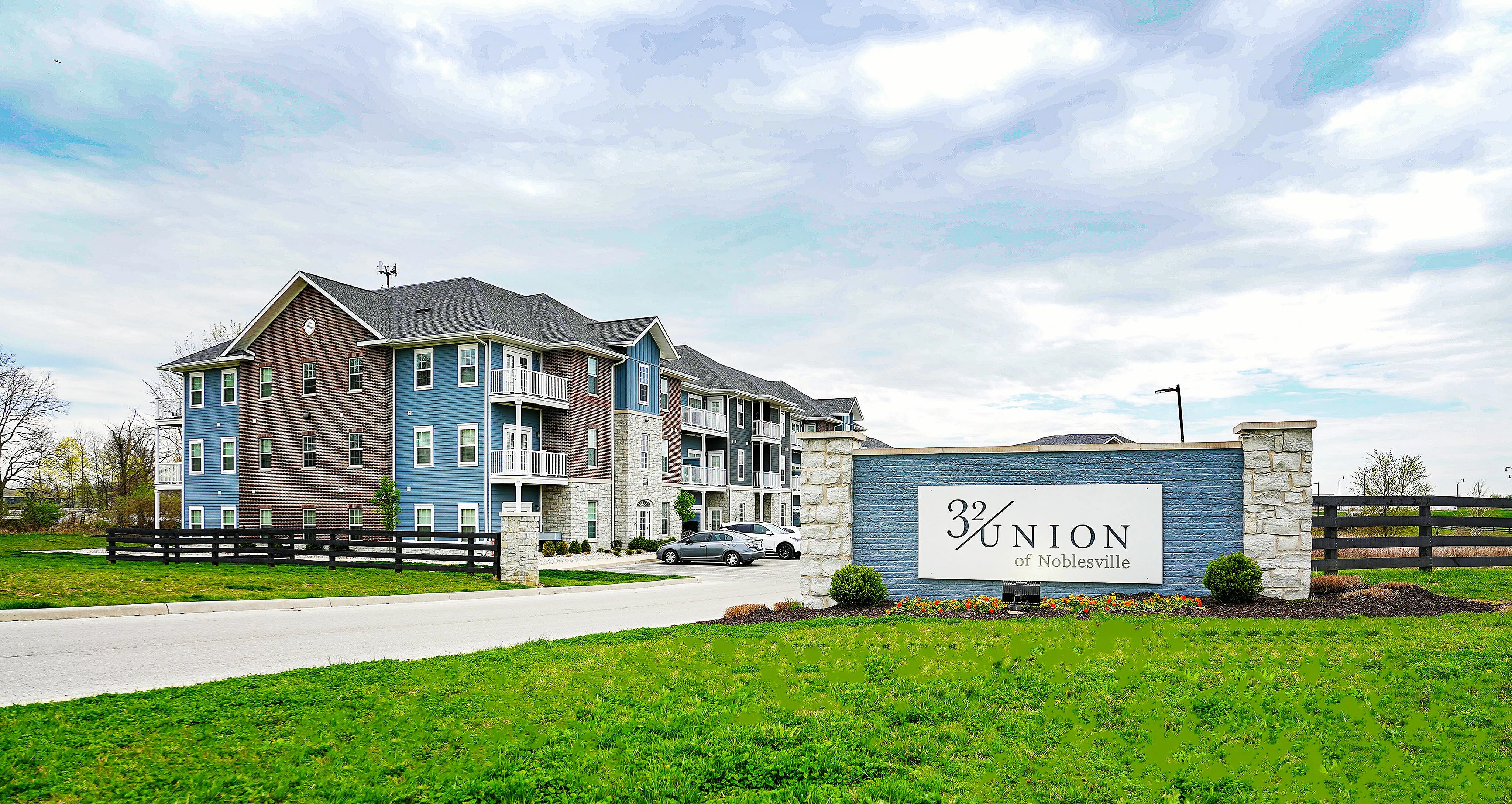 Charming and modern apartment building at 32 Union of Noblesville surrounded by lush greenery and a spacious parking area.
