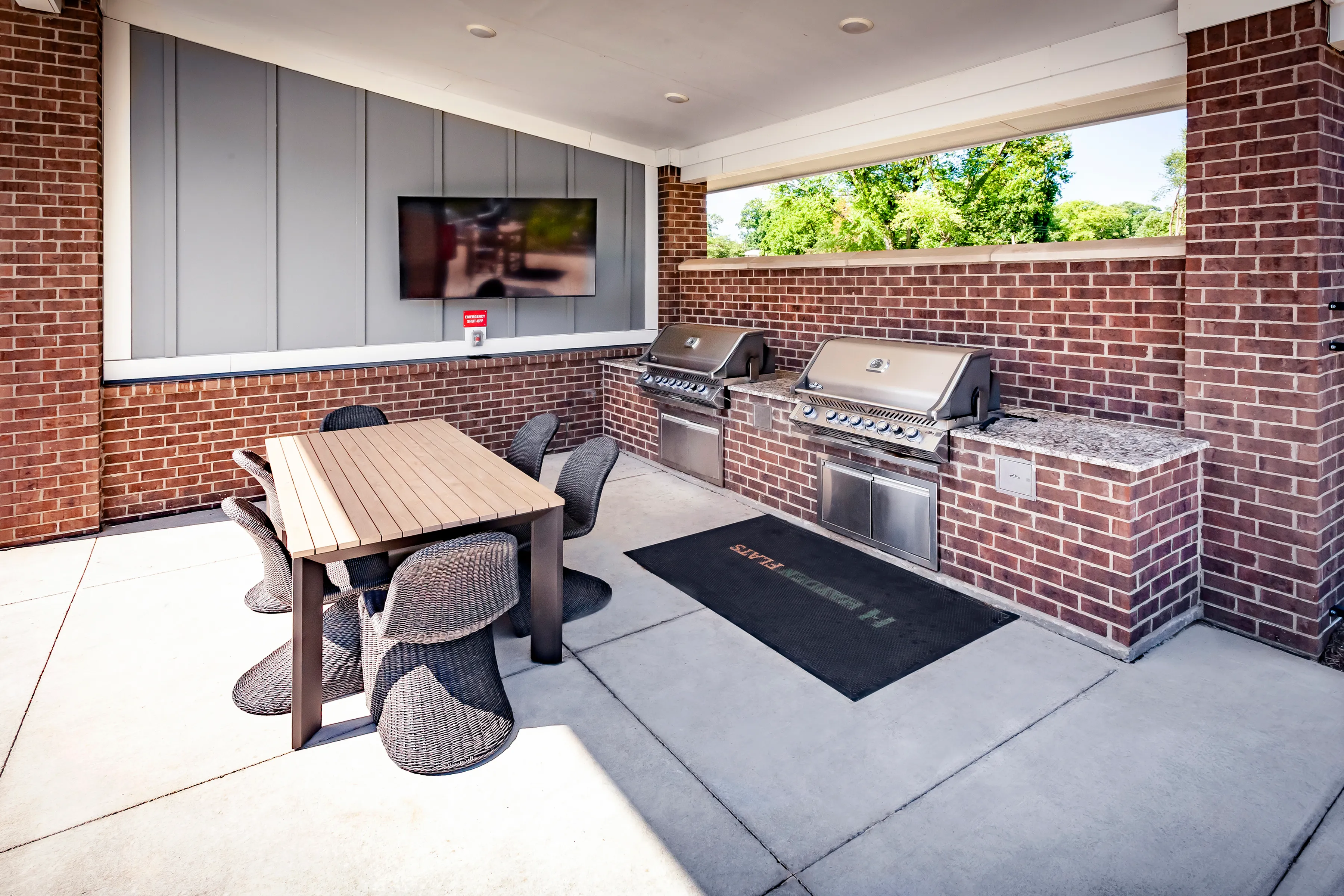 Contemporary outdoor barbecue area featuring sleek grills, a stylish dining table, and comfortable seating beneath a chic mounted TV.