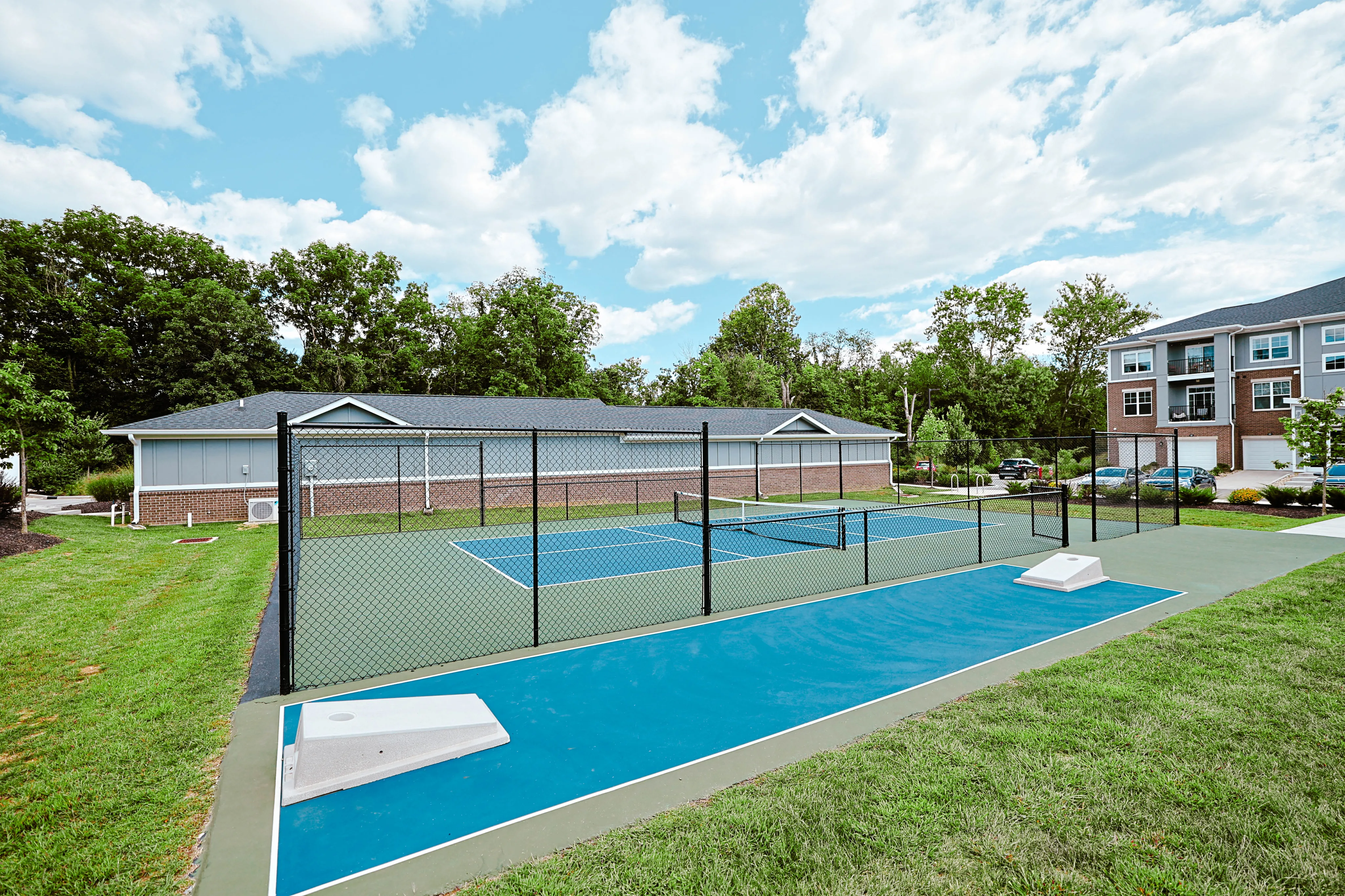 Charming community setting with a vibrant tennis court surrounded by lush greenery and modern buildings.