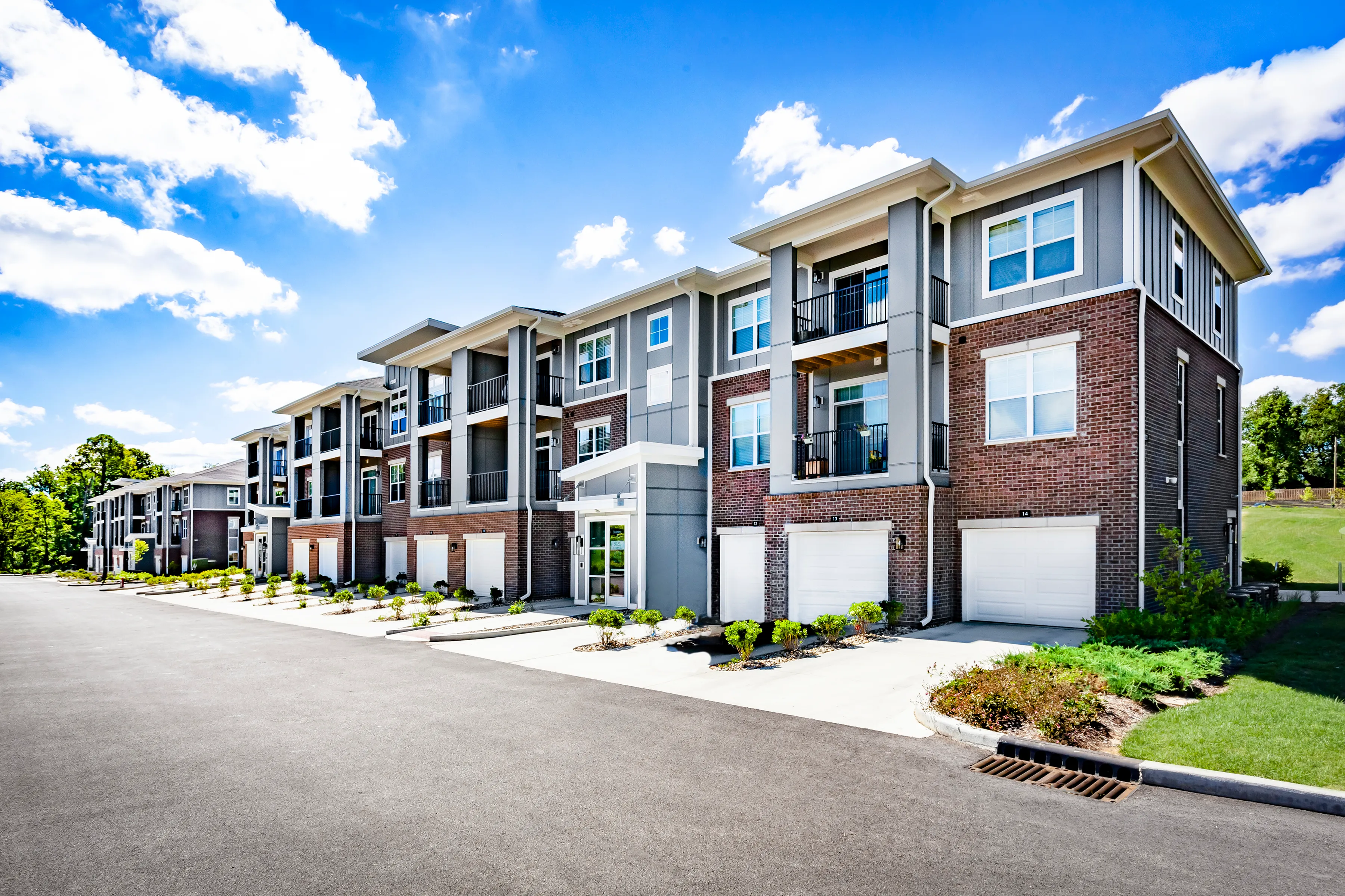 Modern exterior of a stylish apartment complex featuring three-story buildings with balconies, elegant brickwork, and manicured landscaping.
