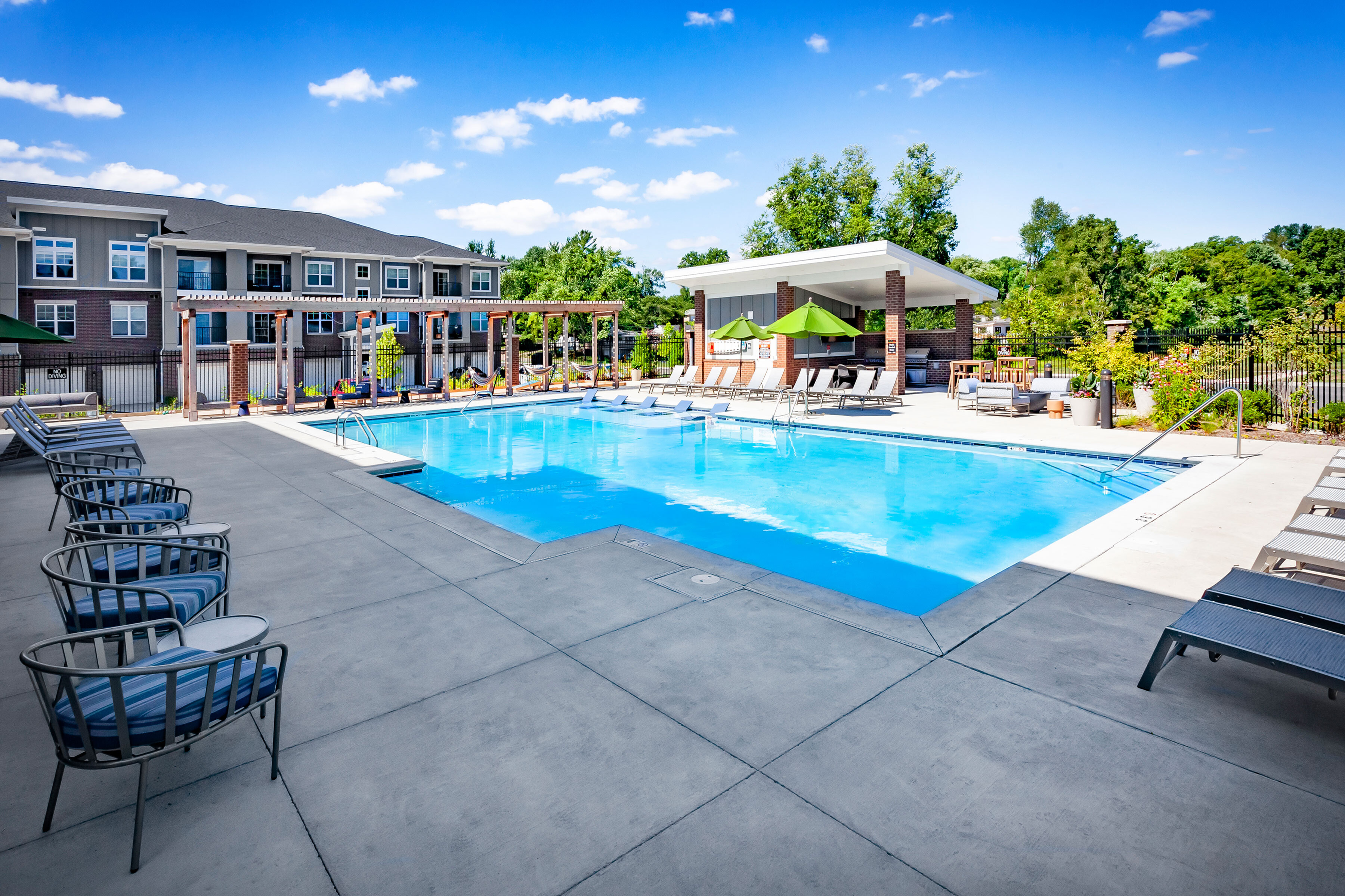 Luxurious apartment complex featuring a sparkling swimming pool with stylish loungers and a modern outdoor lounge area, perfect for relaxation and social gatherings.