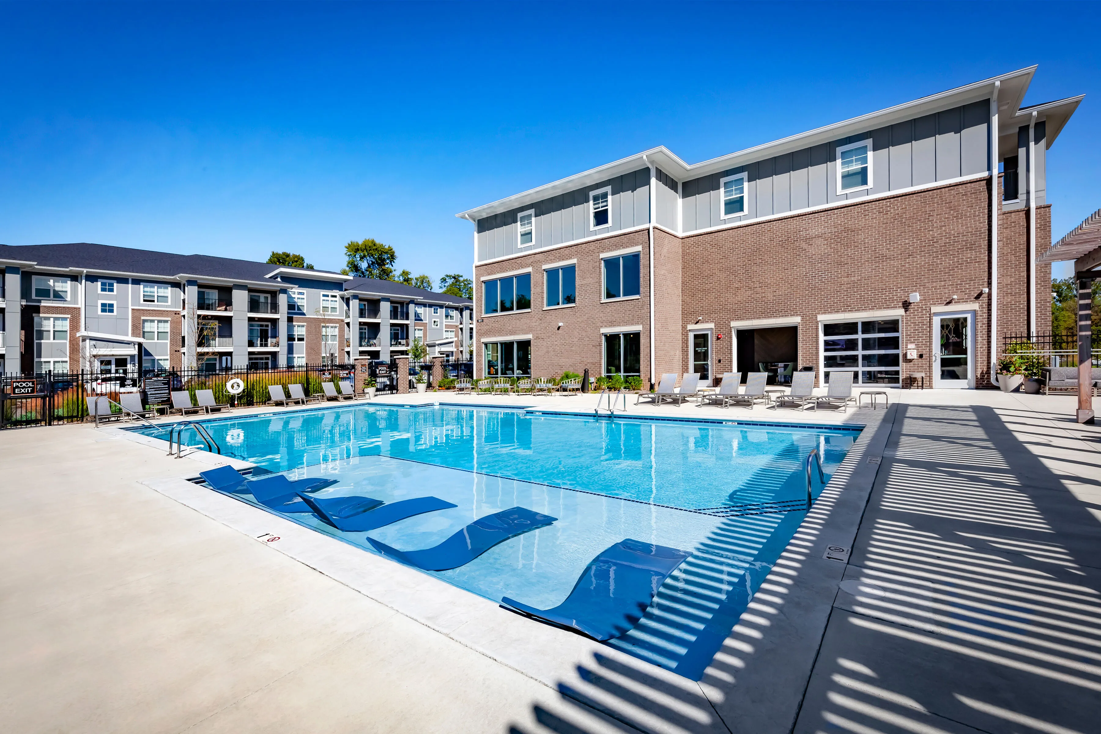 Luxurious looking saltwater pool with in-water loungers next to a partially brick apartment clubhouse.