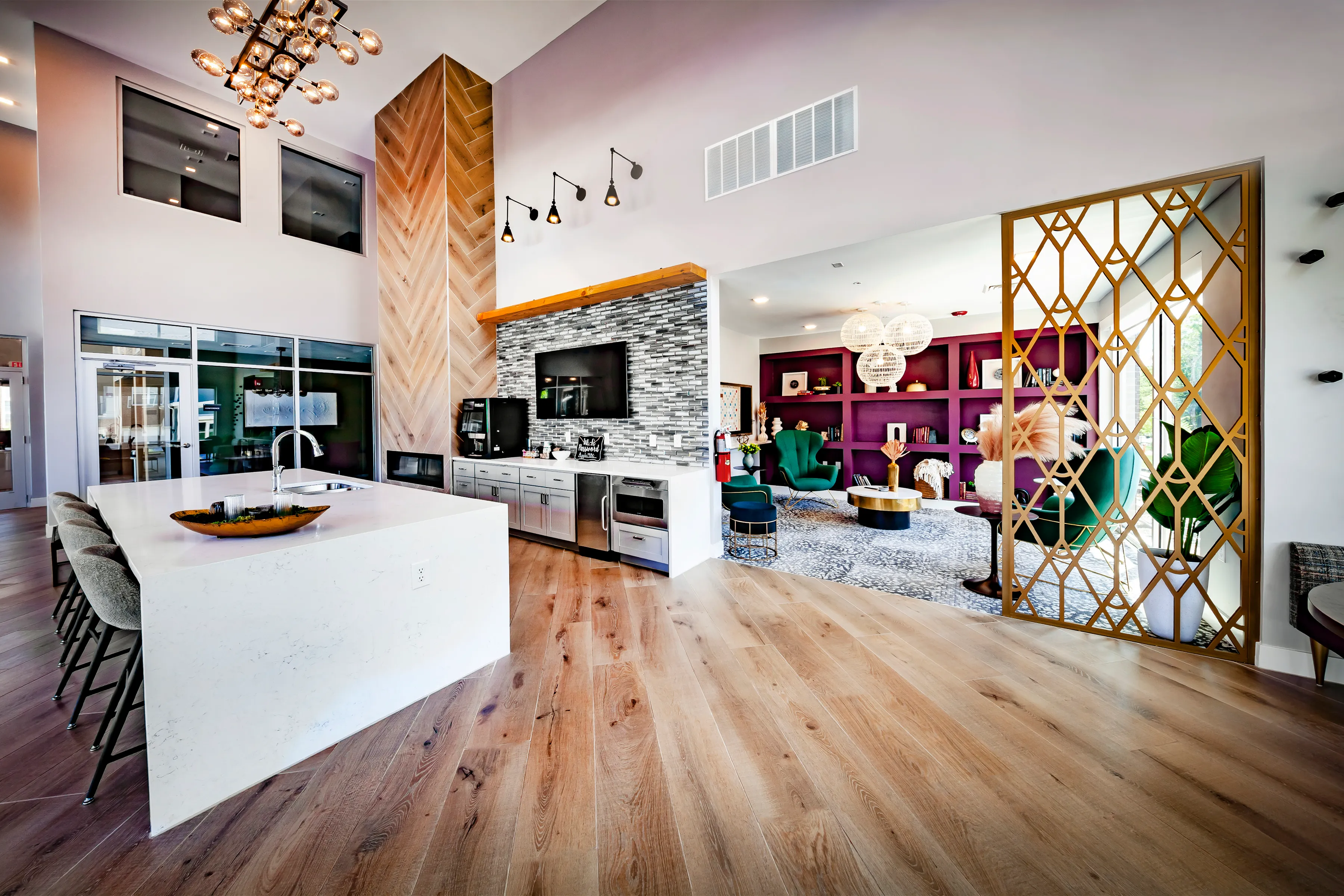 Luxurious open-plan living space featuring a modern kitchen with a sleek island, stylish stone backsplash, and elegant wood flooring, leading to a cozy lounge area with vibrant decor and bold shelving.