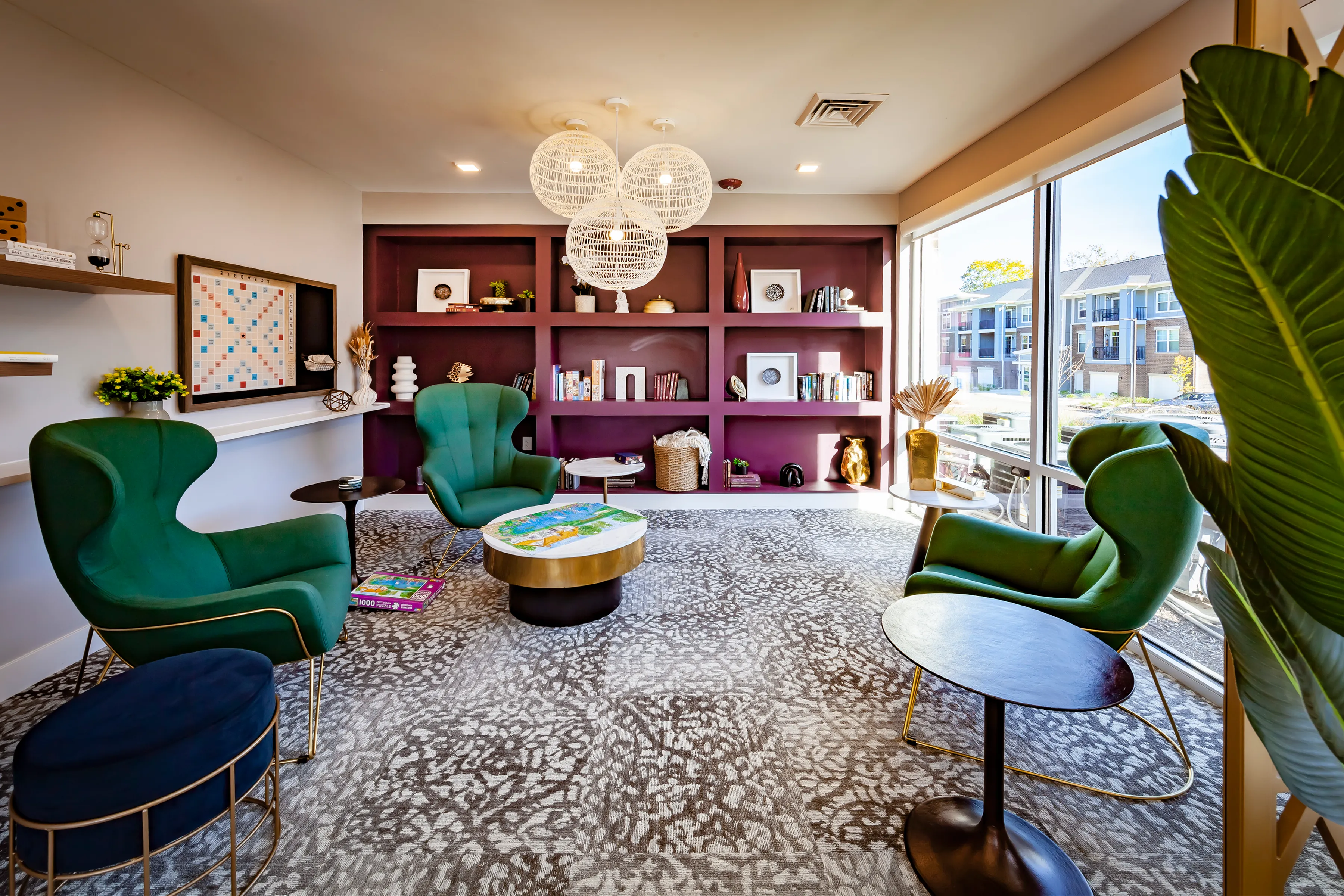 Inviting lounge area with elegant green chairs, vibrant shelving, and large windows offering natural light.