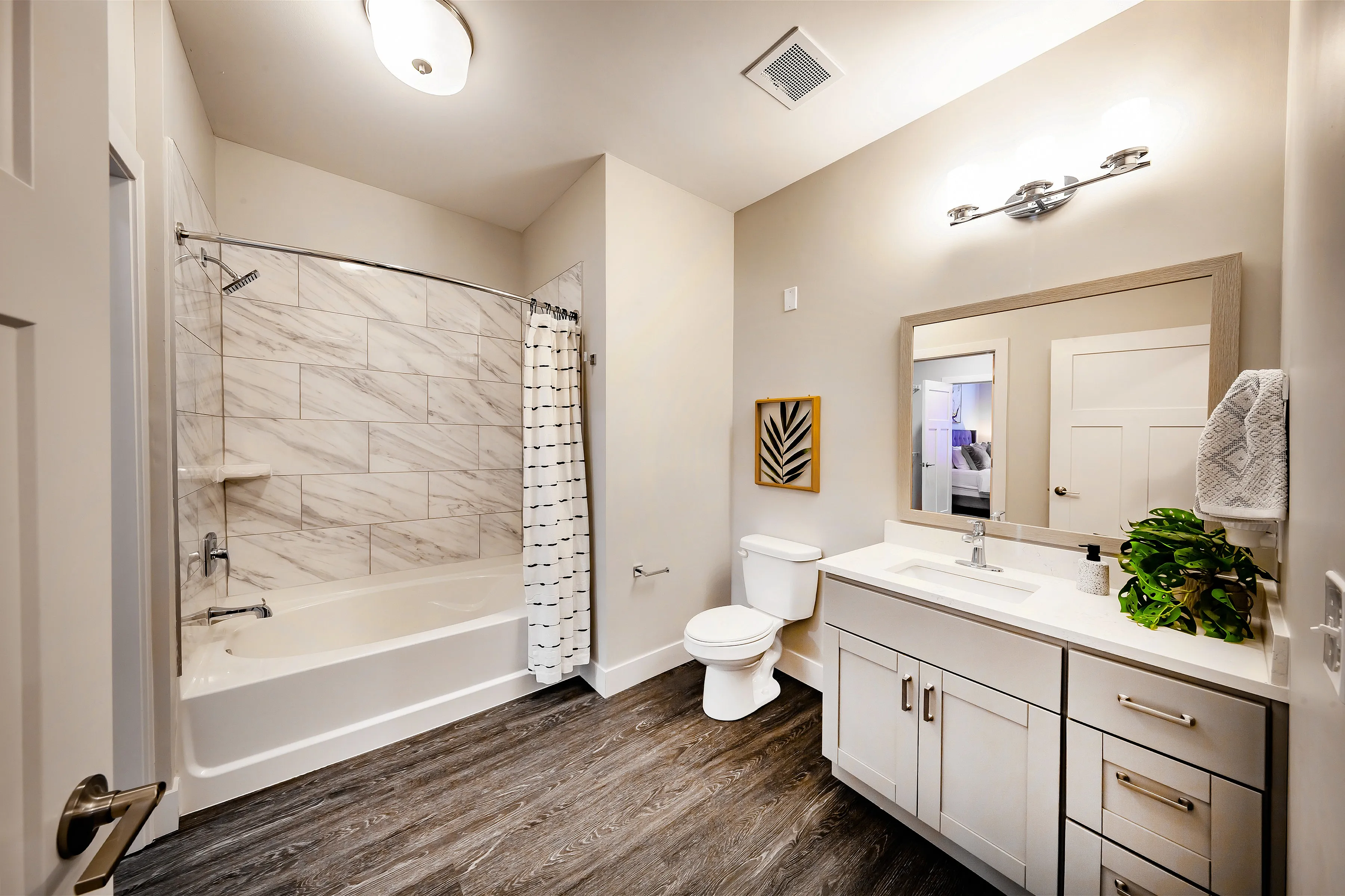 Modern bathroom with elegant wood flooring, stylish marble-tiled bathtub, sleek vanity, and warm accent lighting.