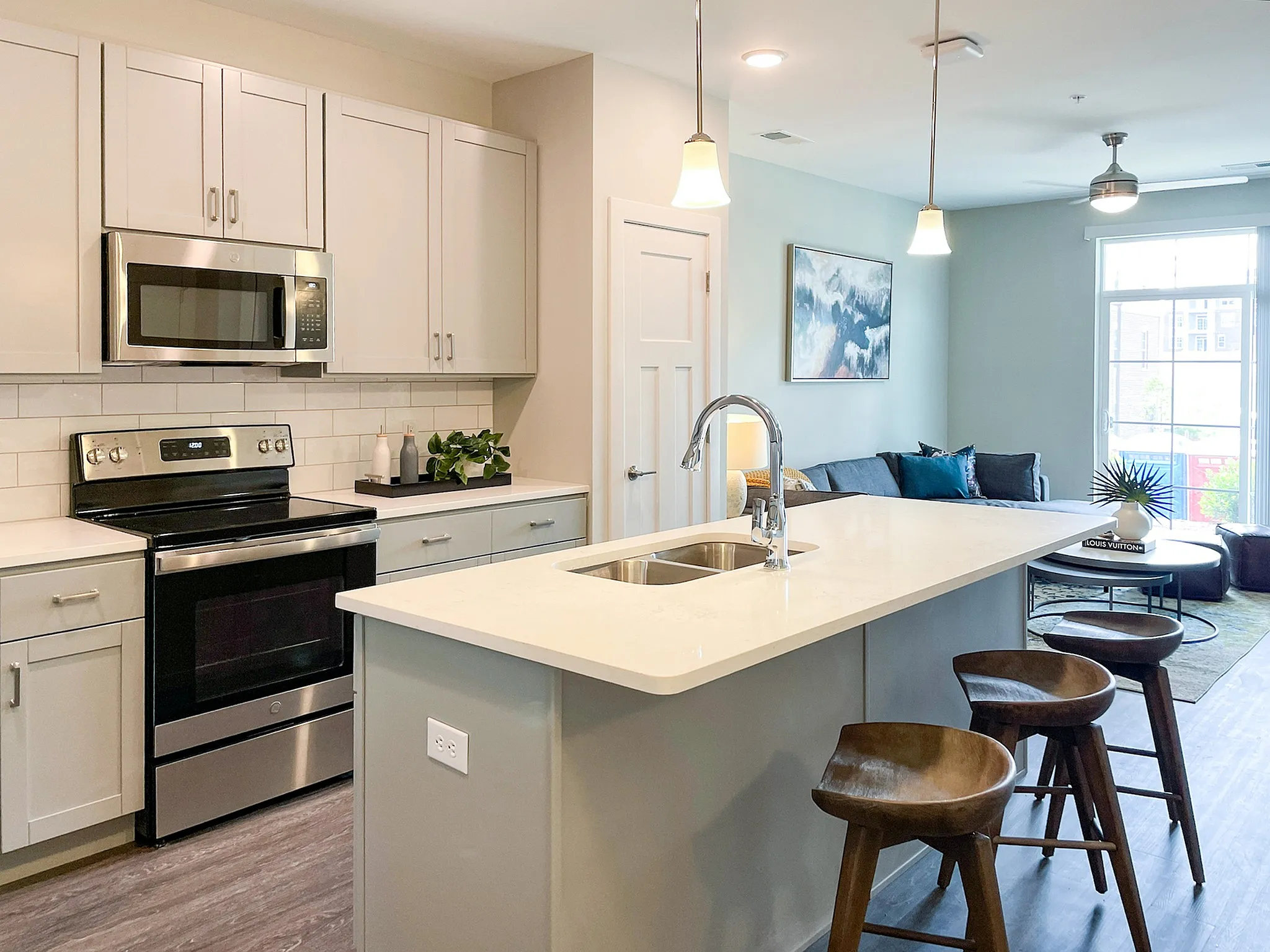 Modern open-concept kitchen and living area featuring sleek cabinetry, stainless steel appliances, and a chic island with stylish bar stools.