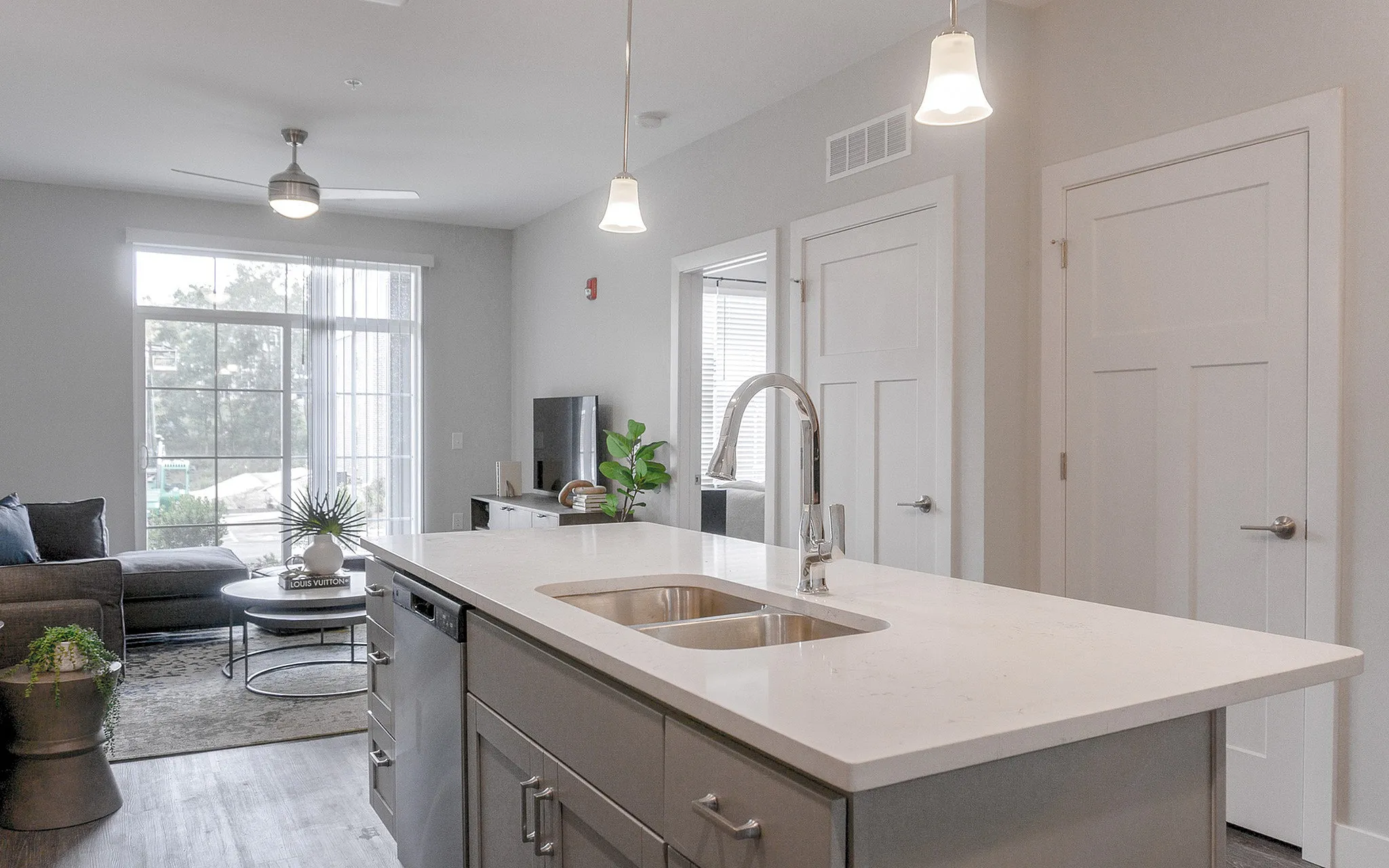 Modern apartment kitchen with sleek countertops, open living space, and floor-to-ceiling windows offering abundant natural light.