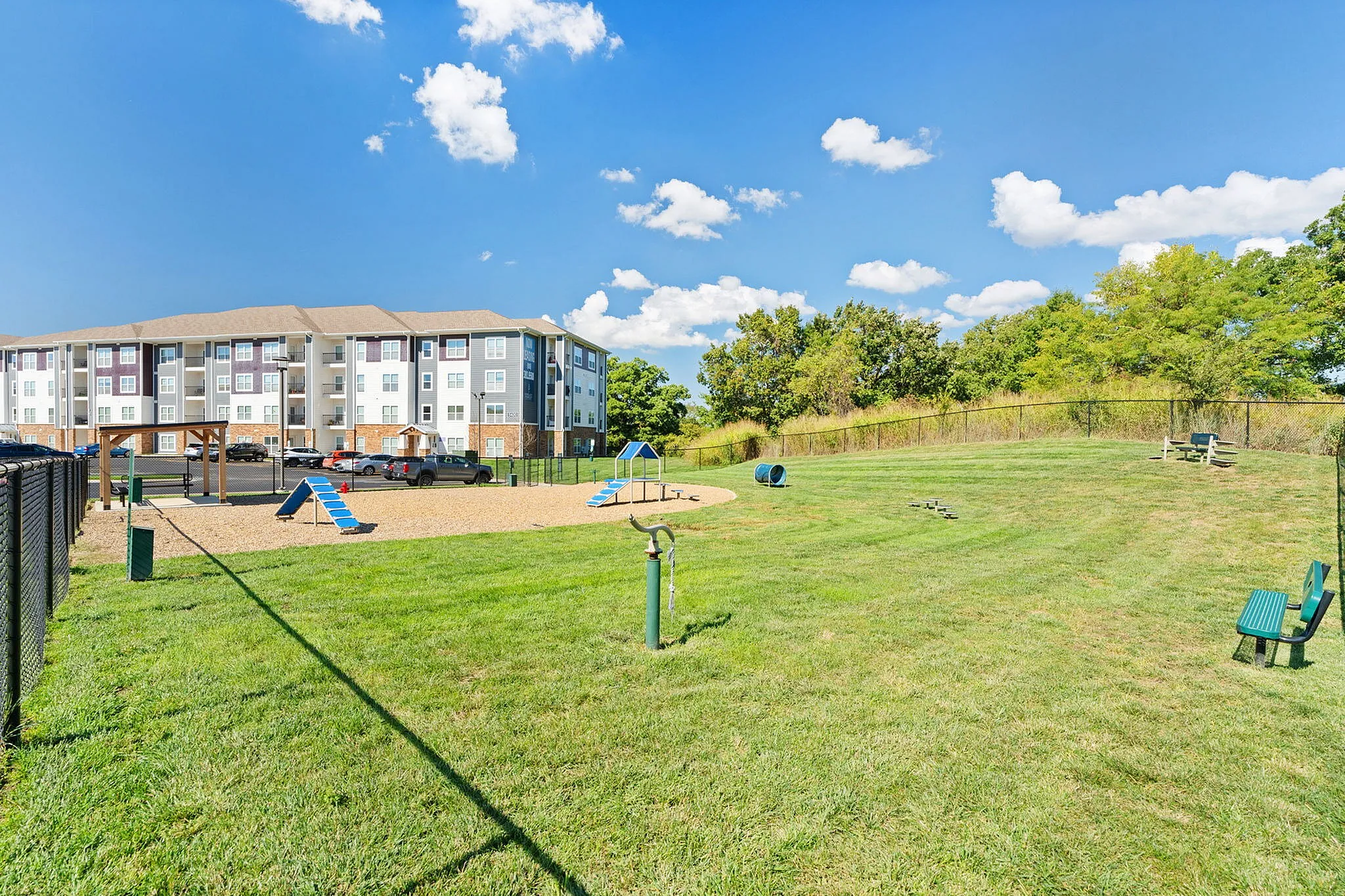 Inviting apartment complex with a vibrant playground, ample parking, and lush green views under a clear blue sky.