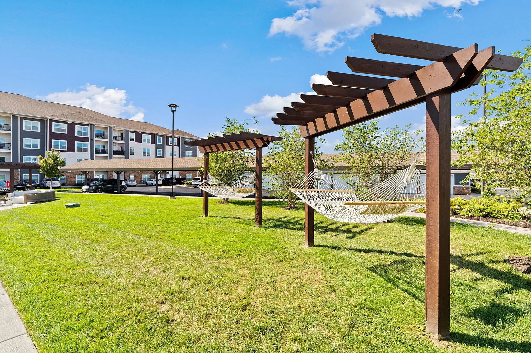 Inviting outdoor space with hammocks under wooden pergolas, perfect for relaxation, set against a modern apartment complex with lush greenery.