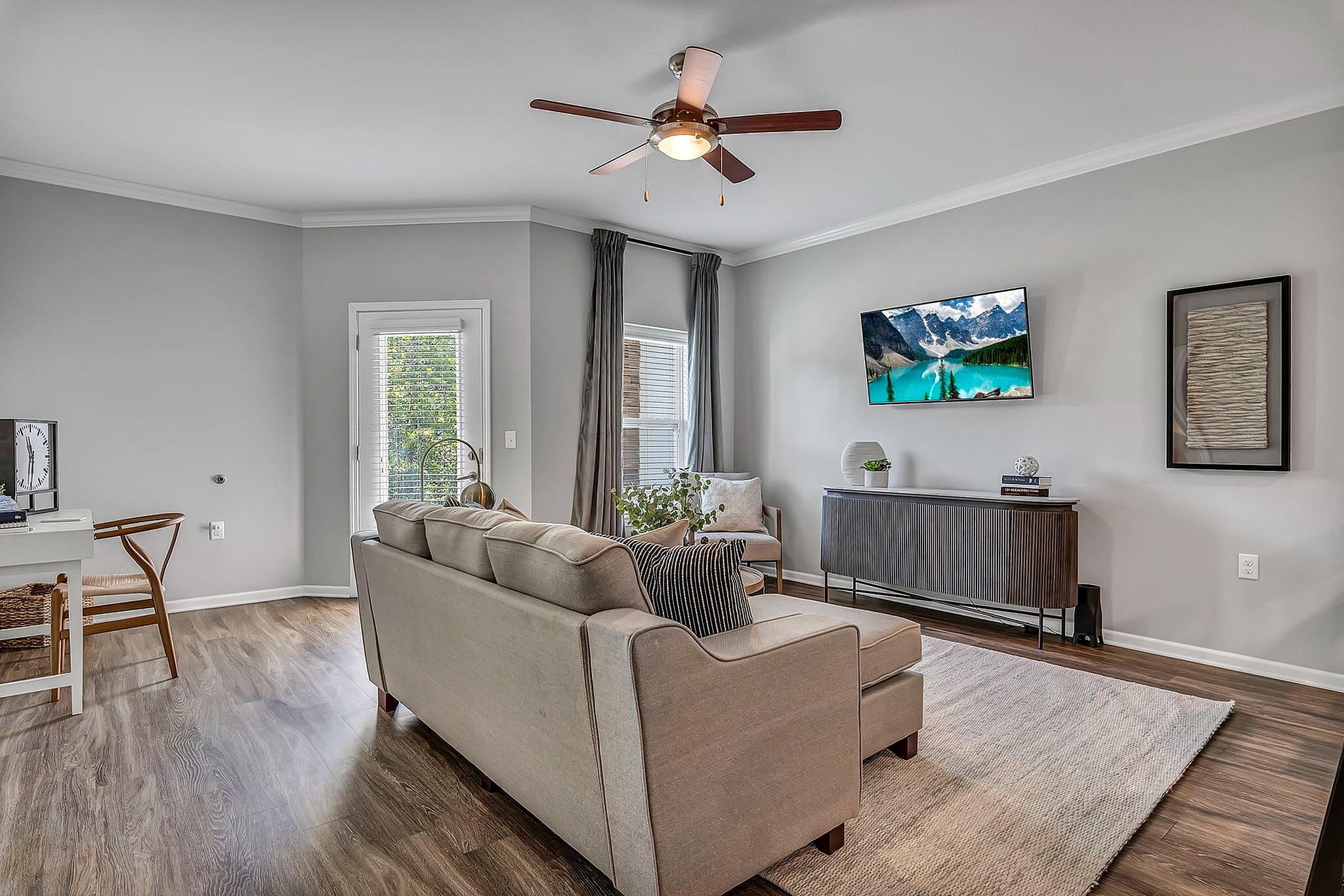 Chic and modern living room featuring elegant wooden flooring, a plush beige sofa, wall-mounted TV, and abundant natural light for a cozy ambiance.