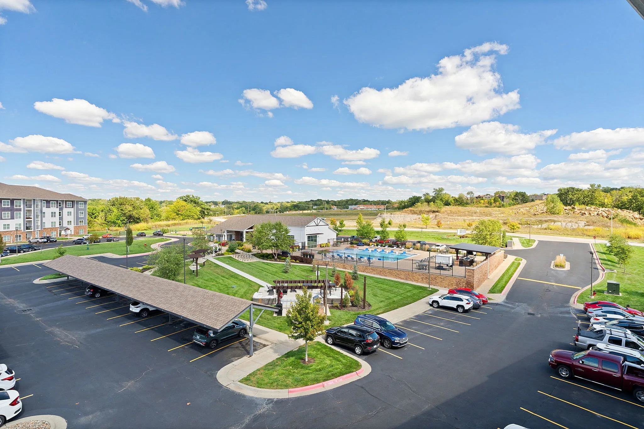 Vibrant apartment complex offering resort-style amenities with a sparkling pool, lush landscaping, and ample parking against a serene blue sky backdrop.